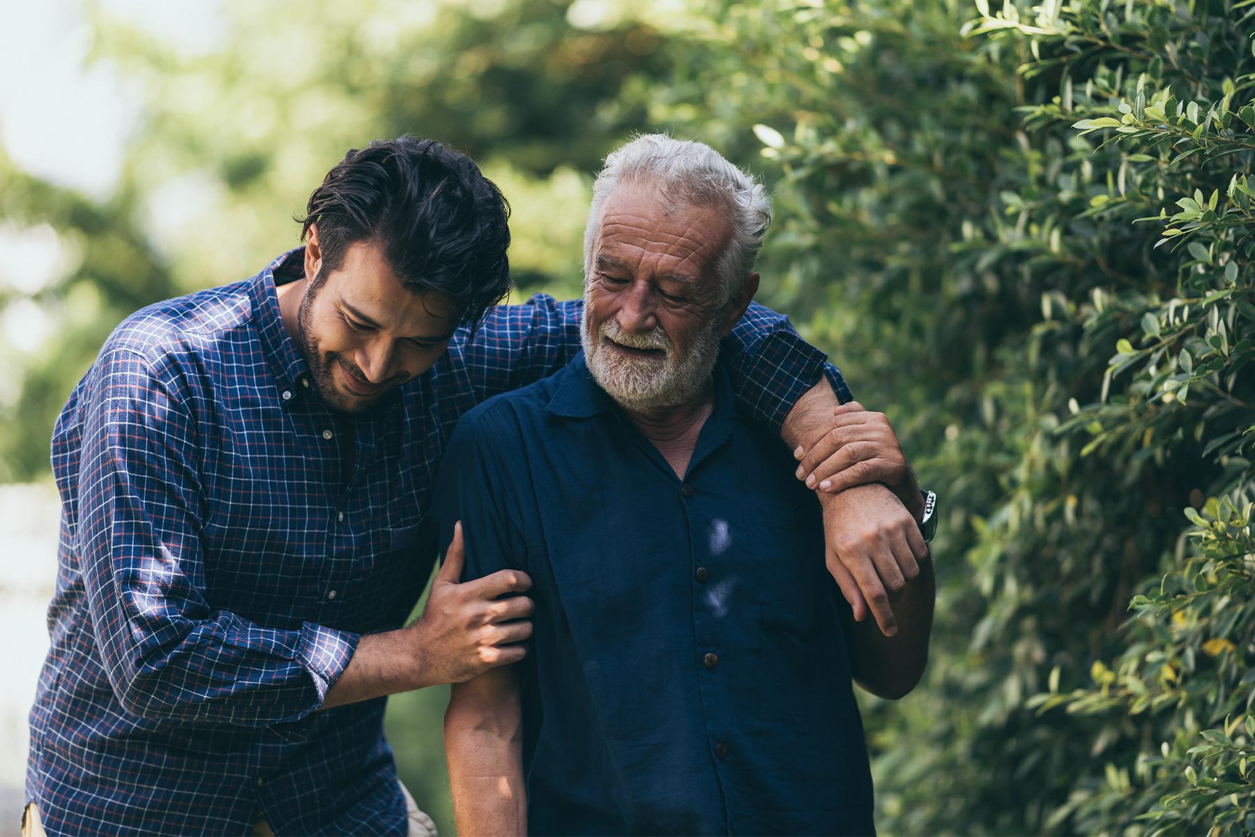 Son with arm around father as they walk together outside.