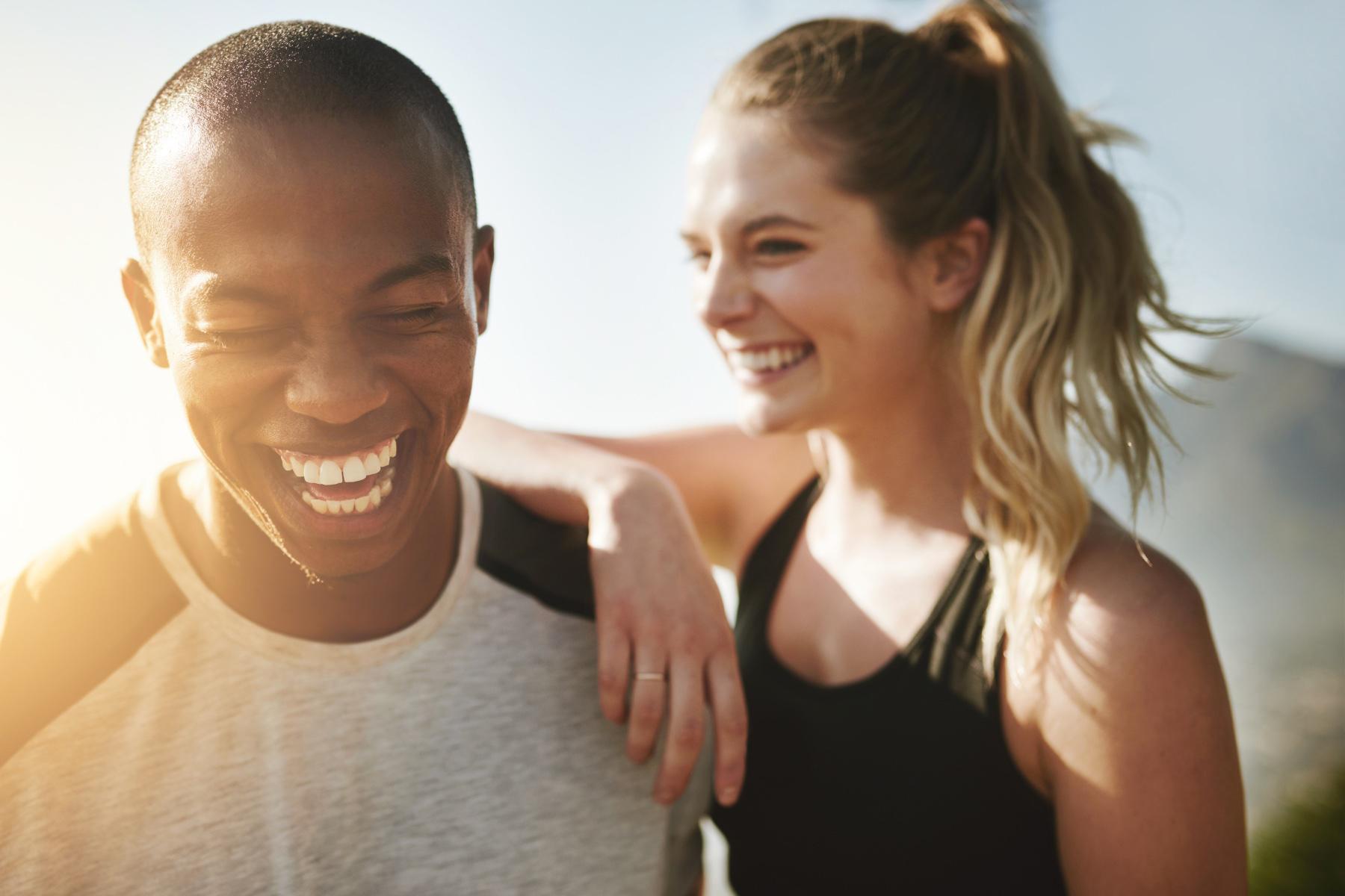 close-up on a smiling young man and woman as she leans her arm on his shoulder