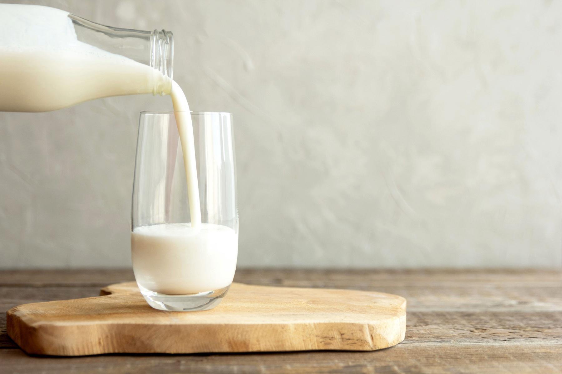 Milk being poured from glass bottle to glass cup.