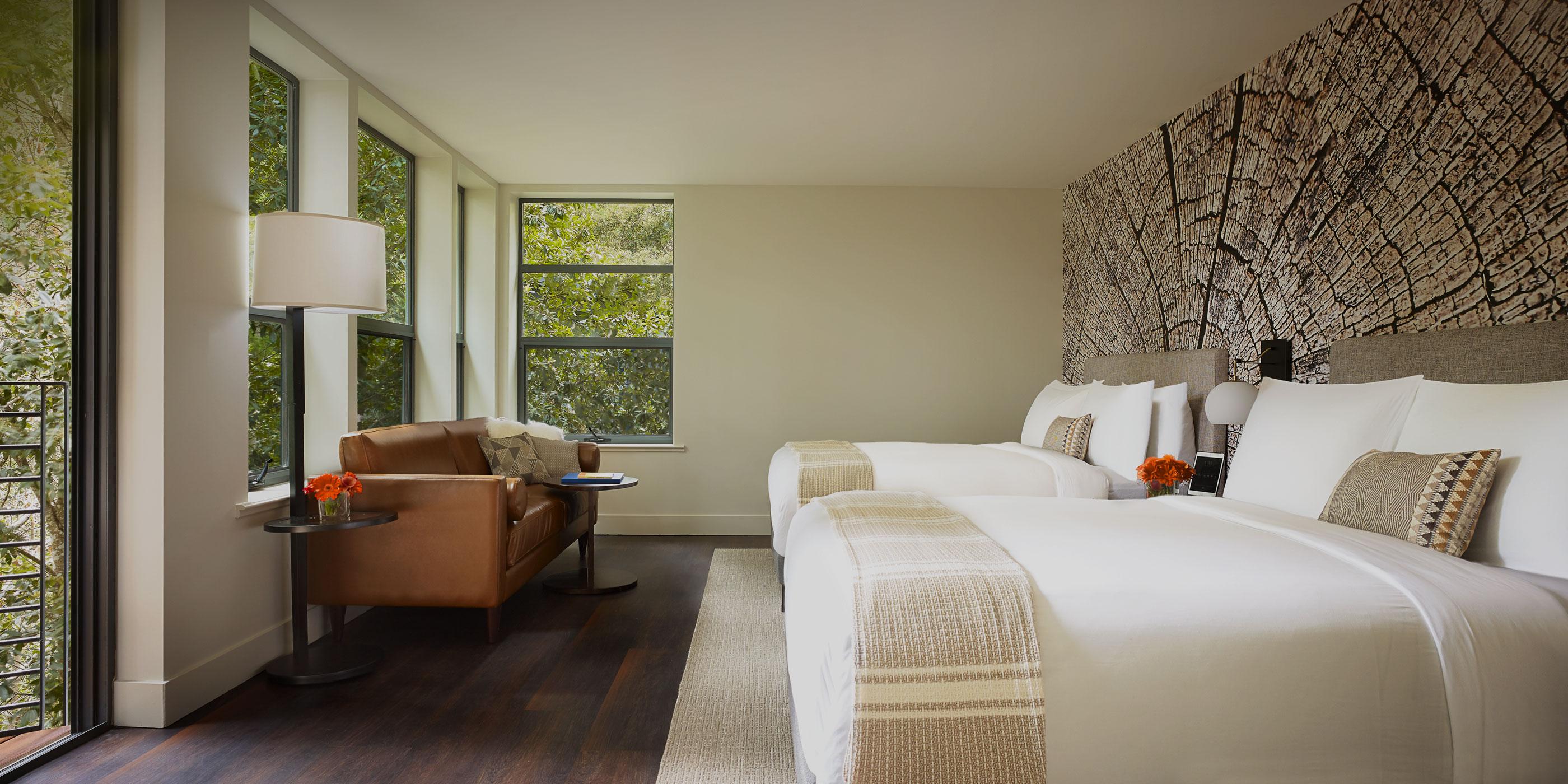 A treehouse room that has a white linen-covered bed in the center of the room, which looks out onto a balcony that is surrounded by trees.
