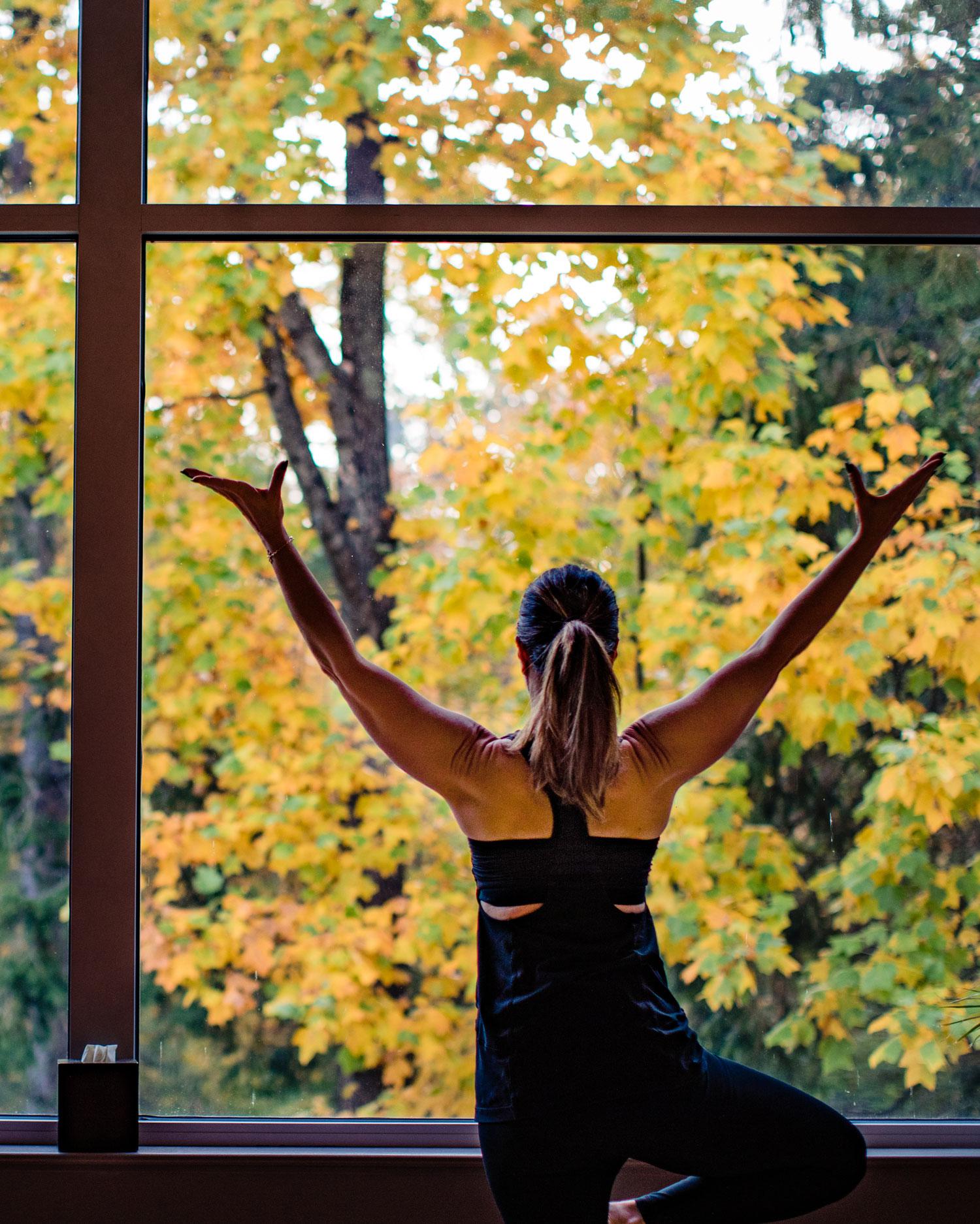 Woman practicing yoga indoors in front of window with beautiful fall colors outside.