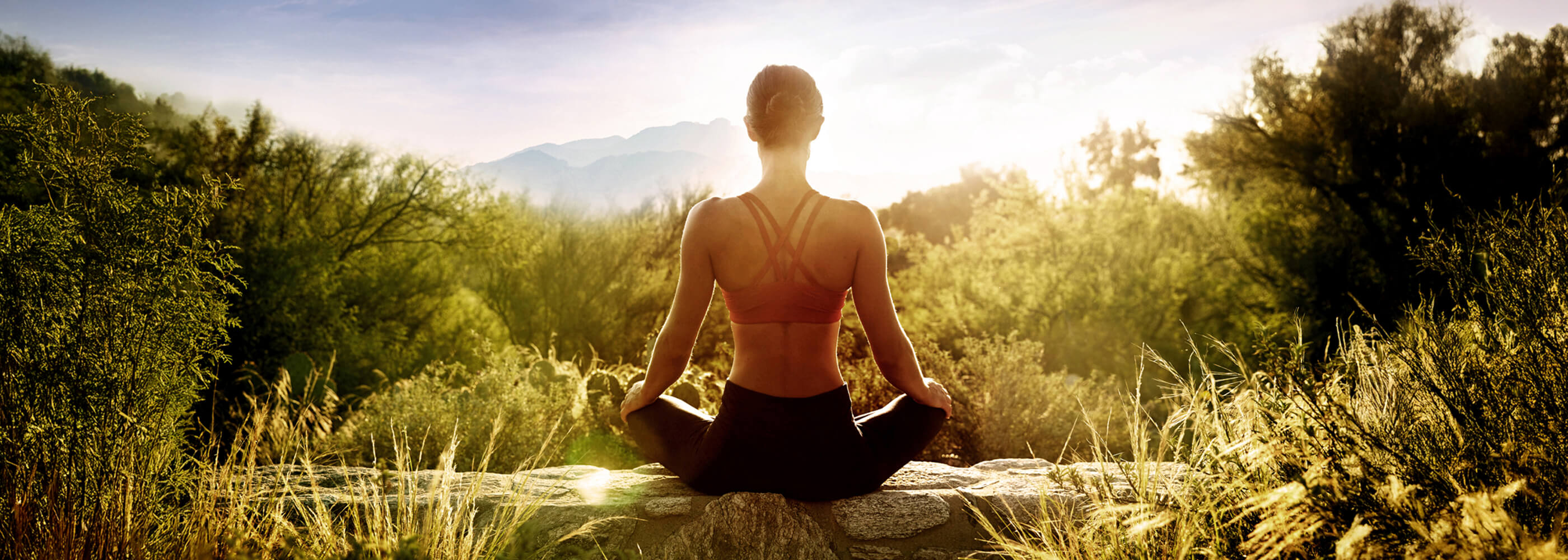 A woman sitting on a wall at sunrise meditating