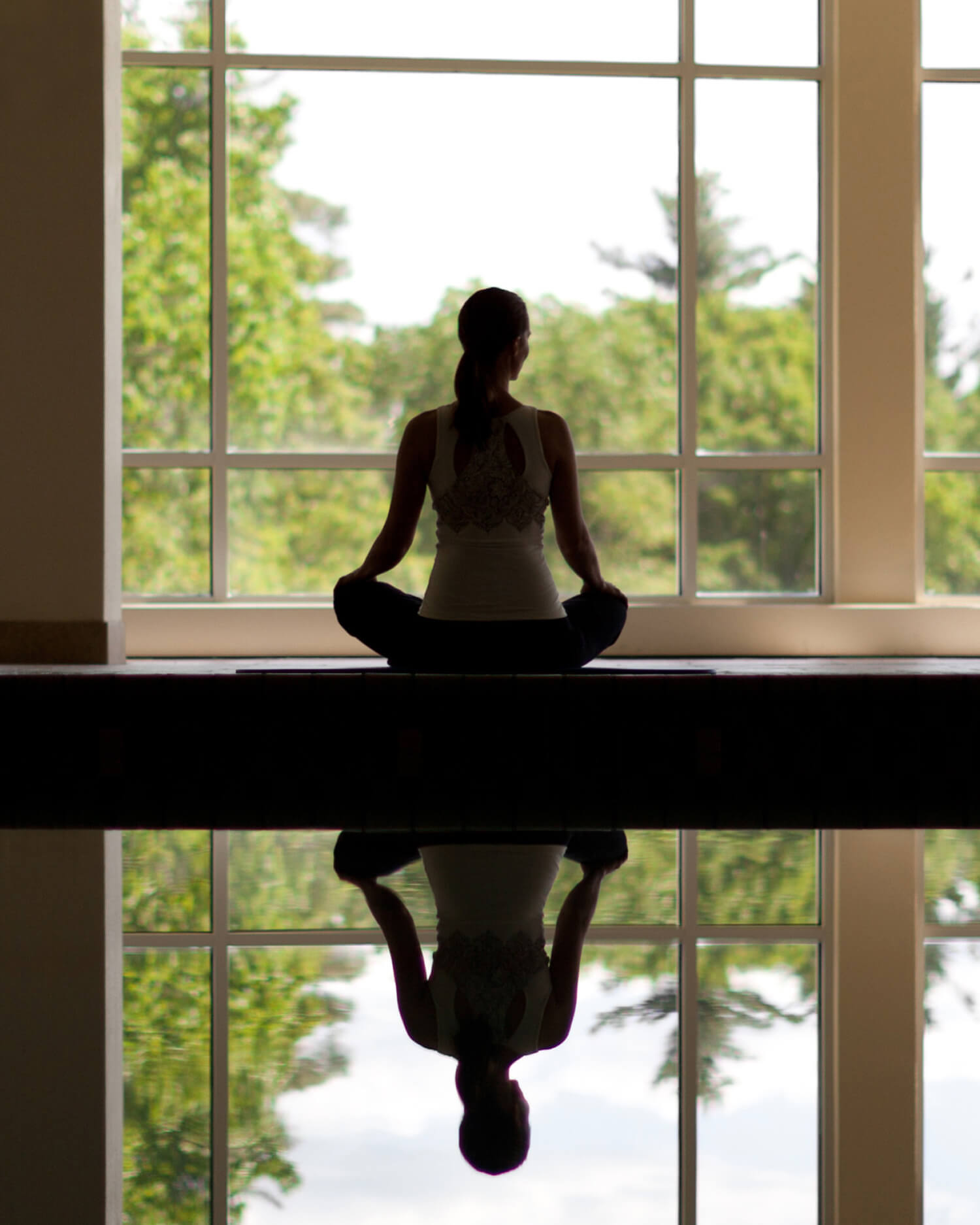A woman sitting next to an indoor swimming pool meditating