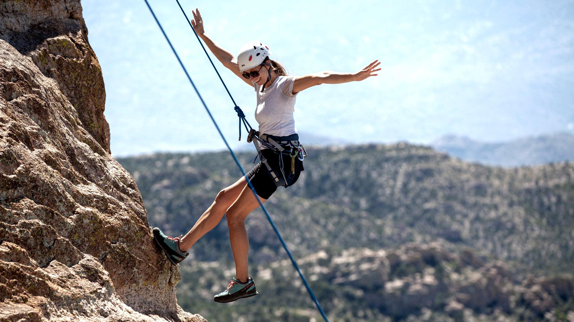 Woman having a great time while mountain climbing on side of rock.