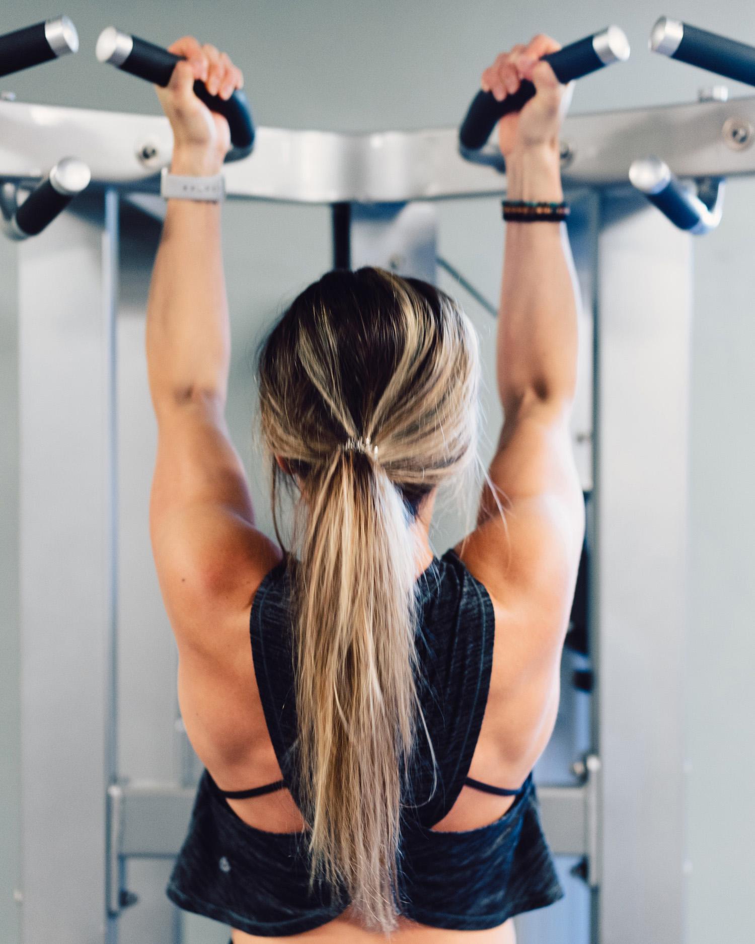 Image of woman's back as she uses lat pulldown machine in gym.