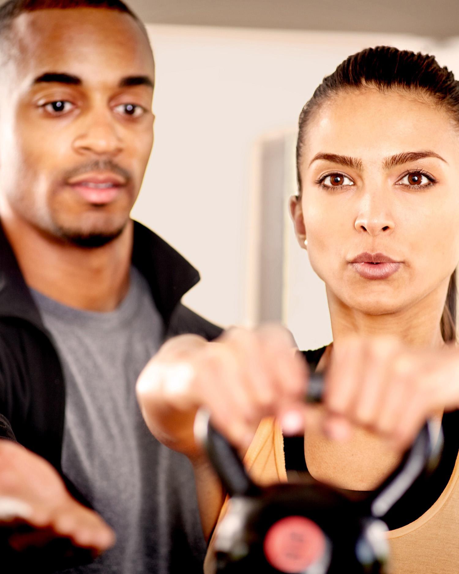Image of man coaching coaching woman during kettlebell lift.