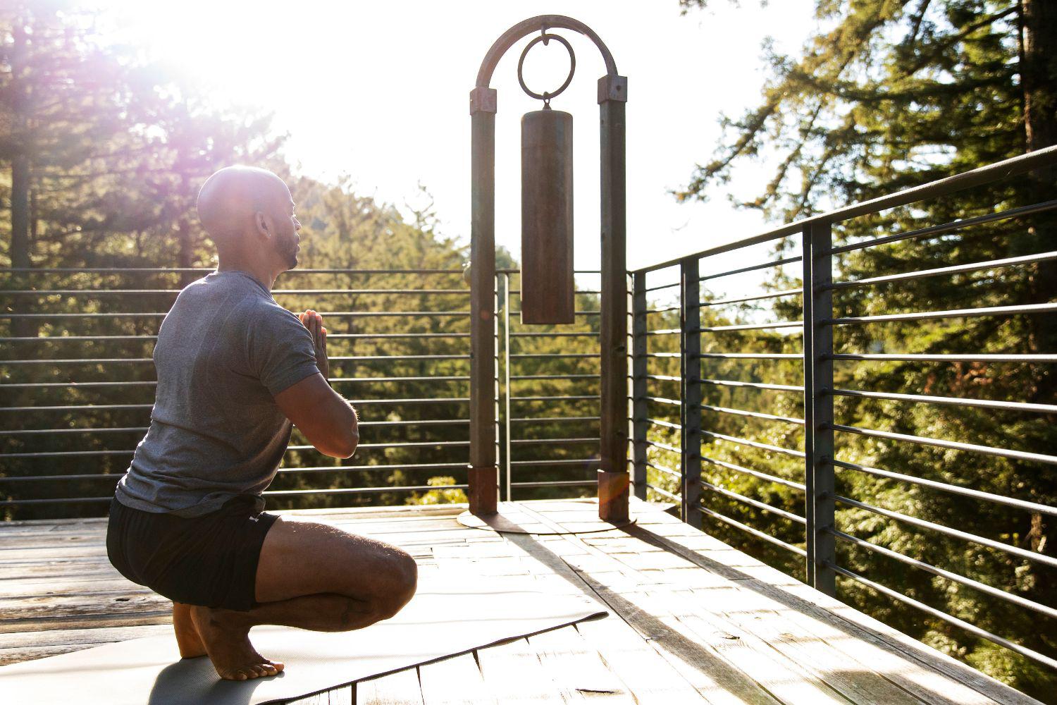 Image of man meditating on deck overlooking Redwood trees at a yoga retreat hosted by Canyon Ranch Woodside Fitness + Spa Resort
