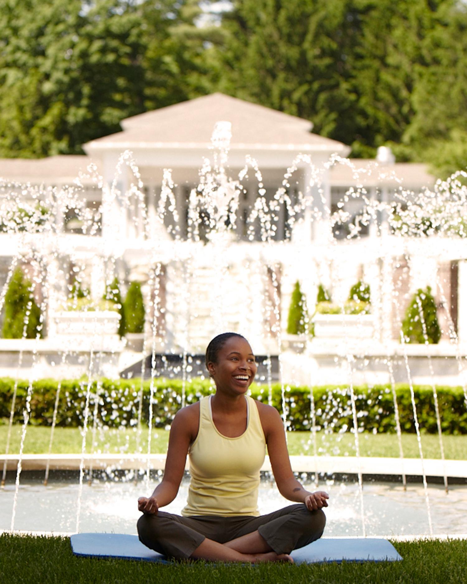 Image of woman doing yoga and smiling while in front of the fountain at Canyon Ranch Lenox.