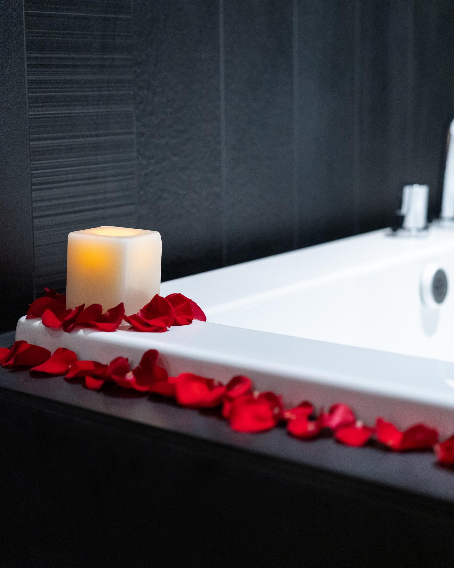 A candle sitting on the edge of a bathtub with rose petals scattered around