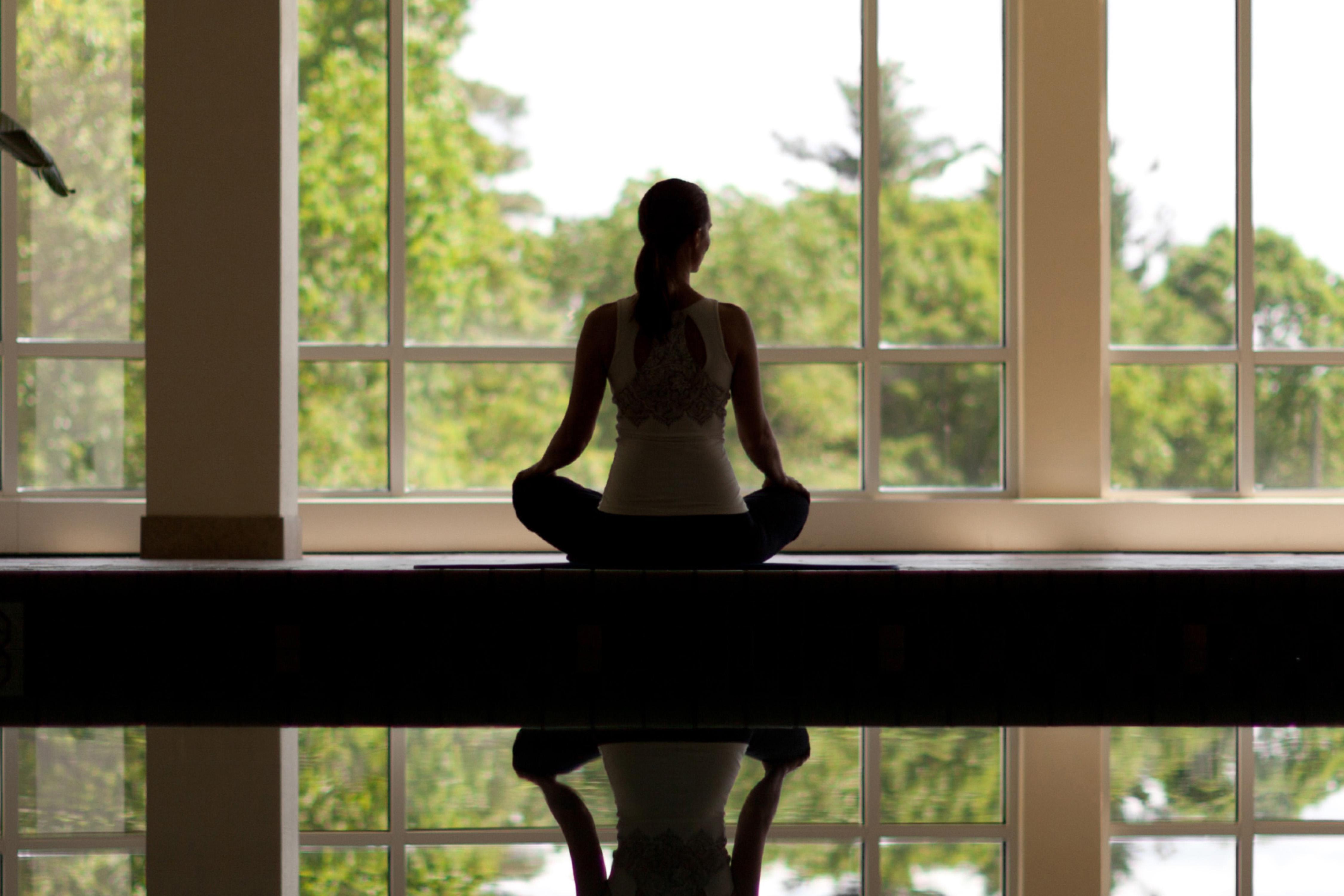 woman meditating in front of large windows