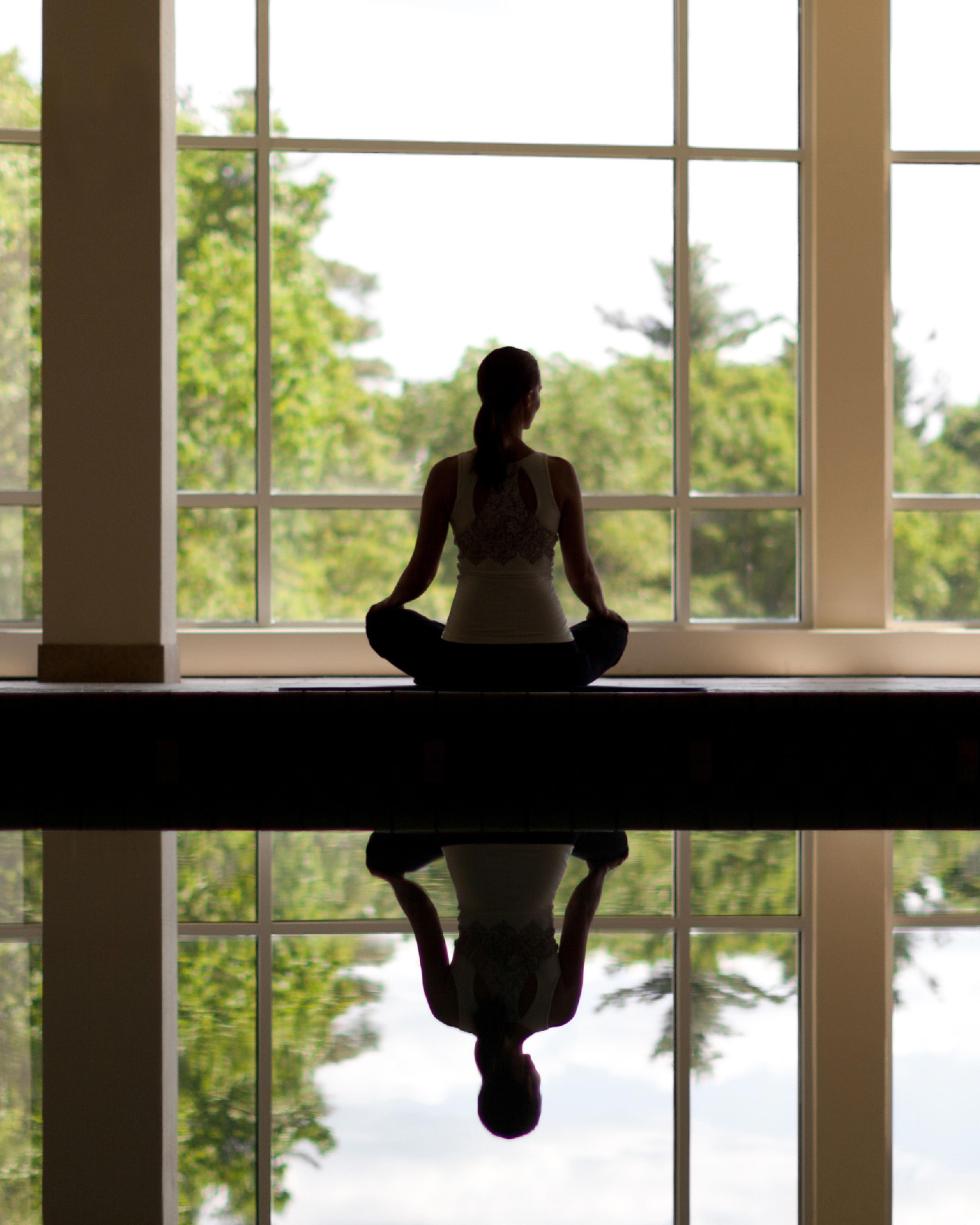 woman meditating in front of large windows