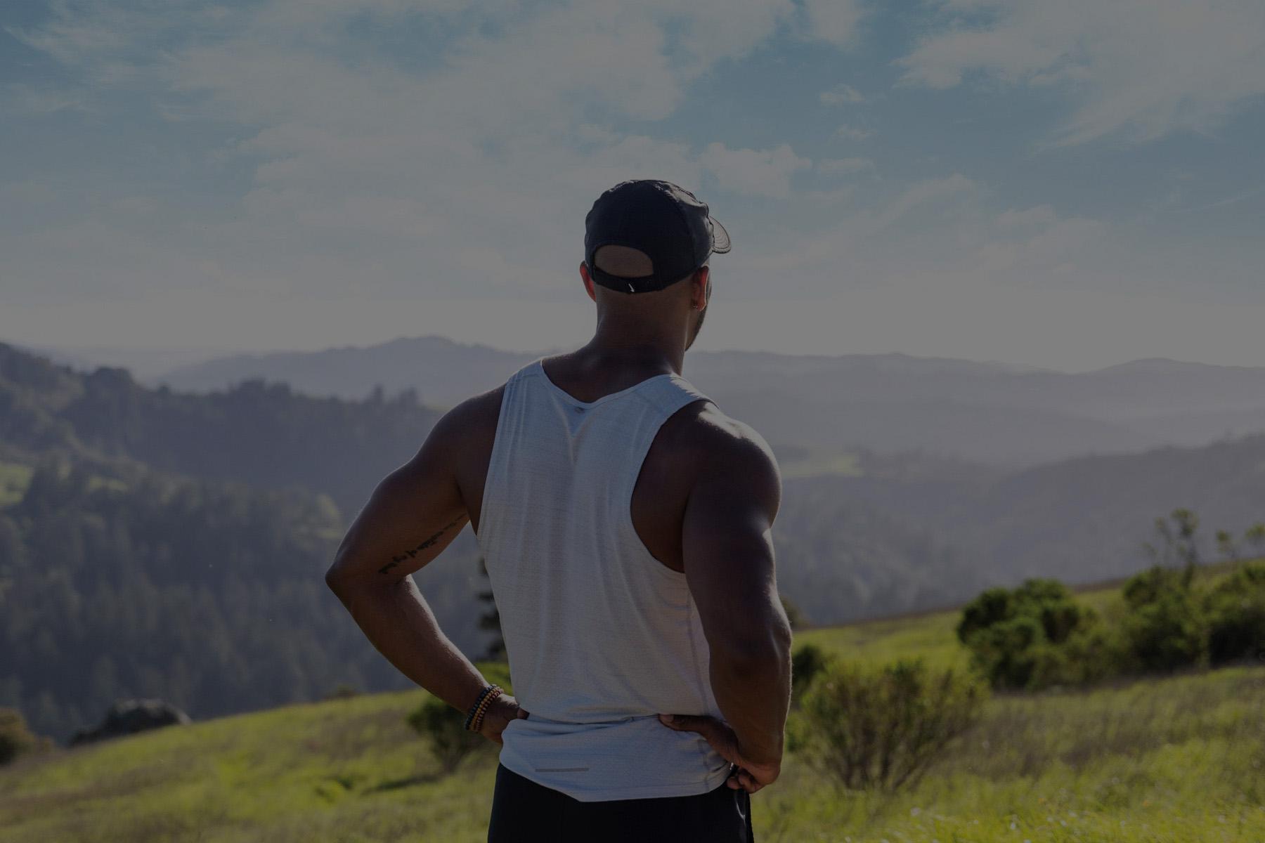 Image of man with hands on hips standing on a mountainside overlooking valley.