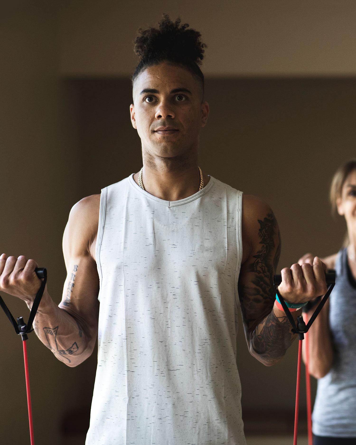 Image of a young man doing bicep curls with a red band at a group fitness class at Canyon Ranch. 