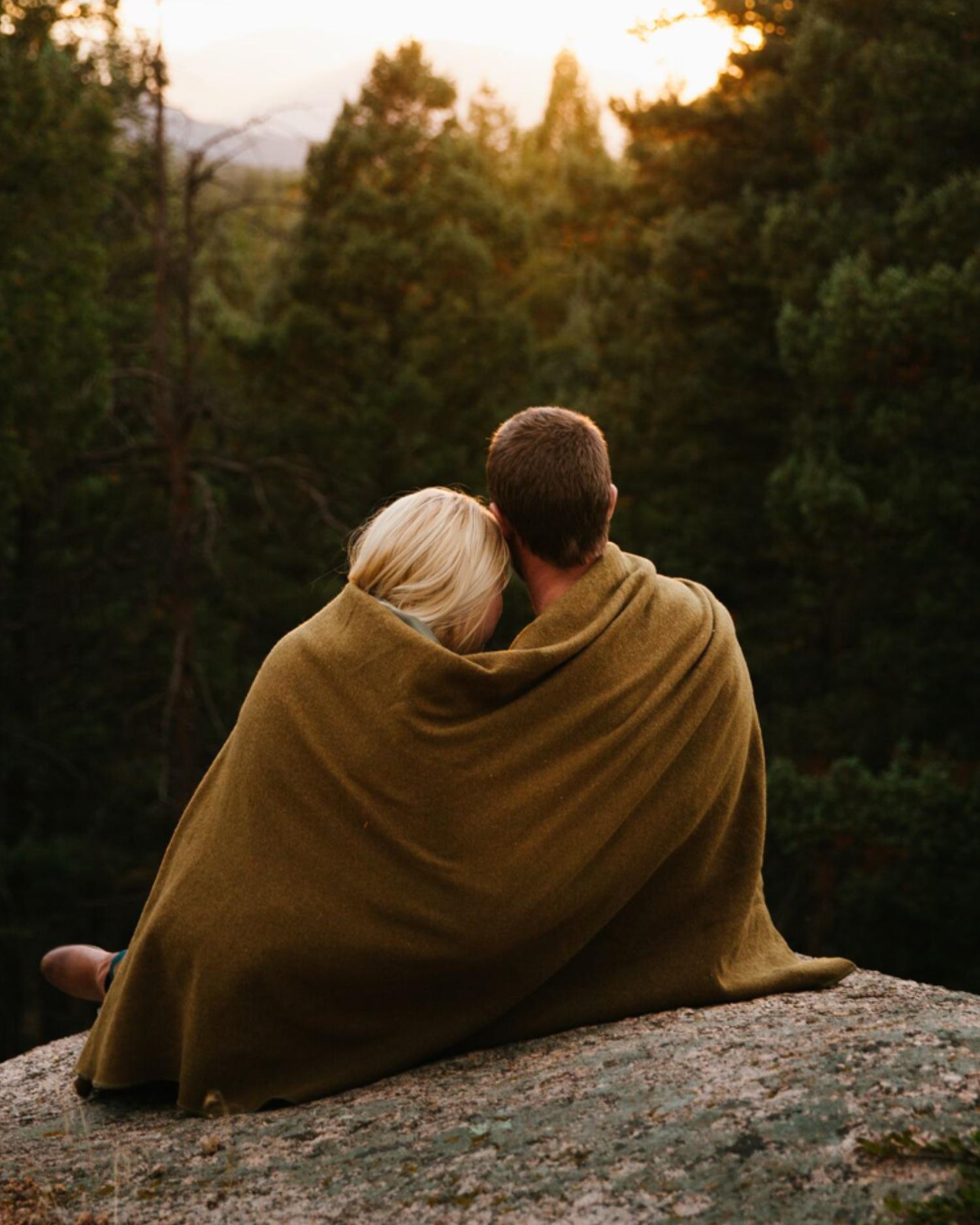 A man and a woman cuddling under a blanket outdoors
