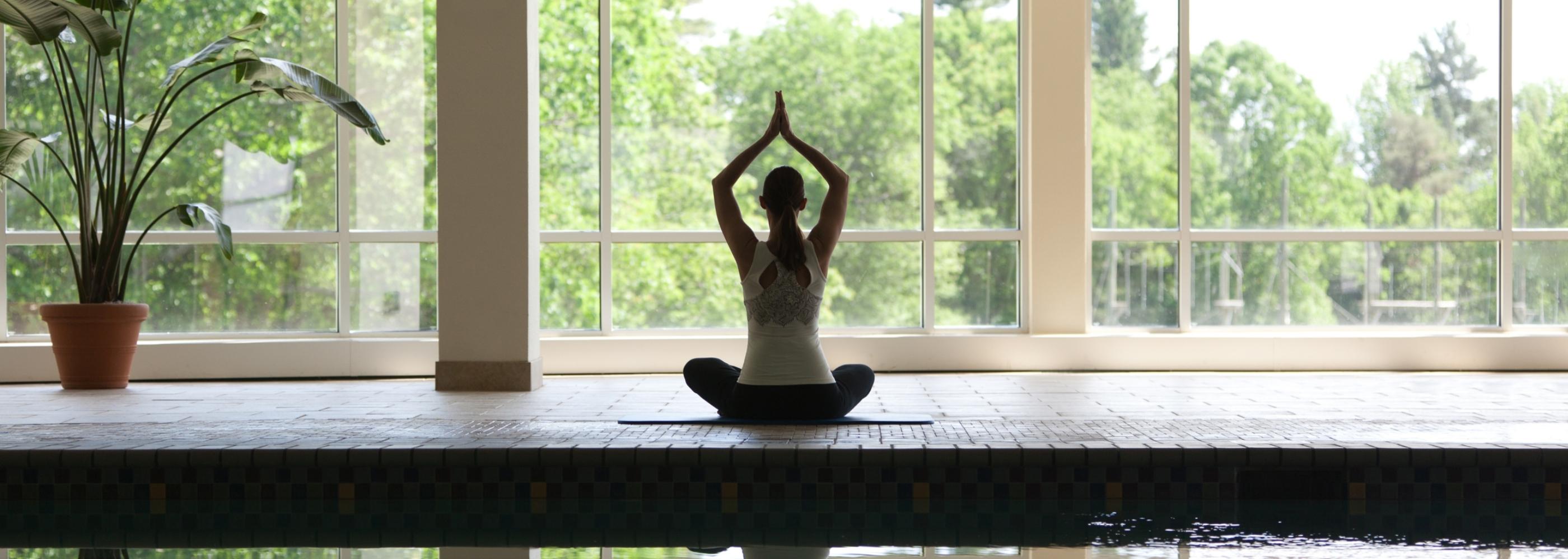 A woman doing yoga by an indoor pool