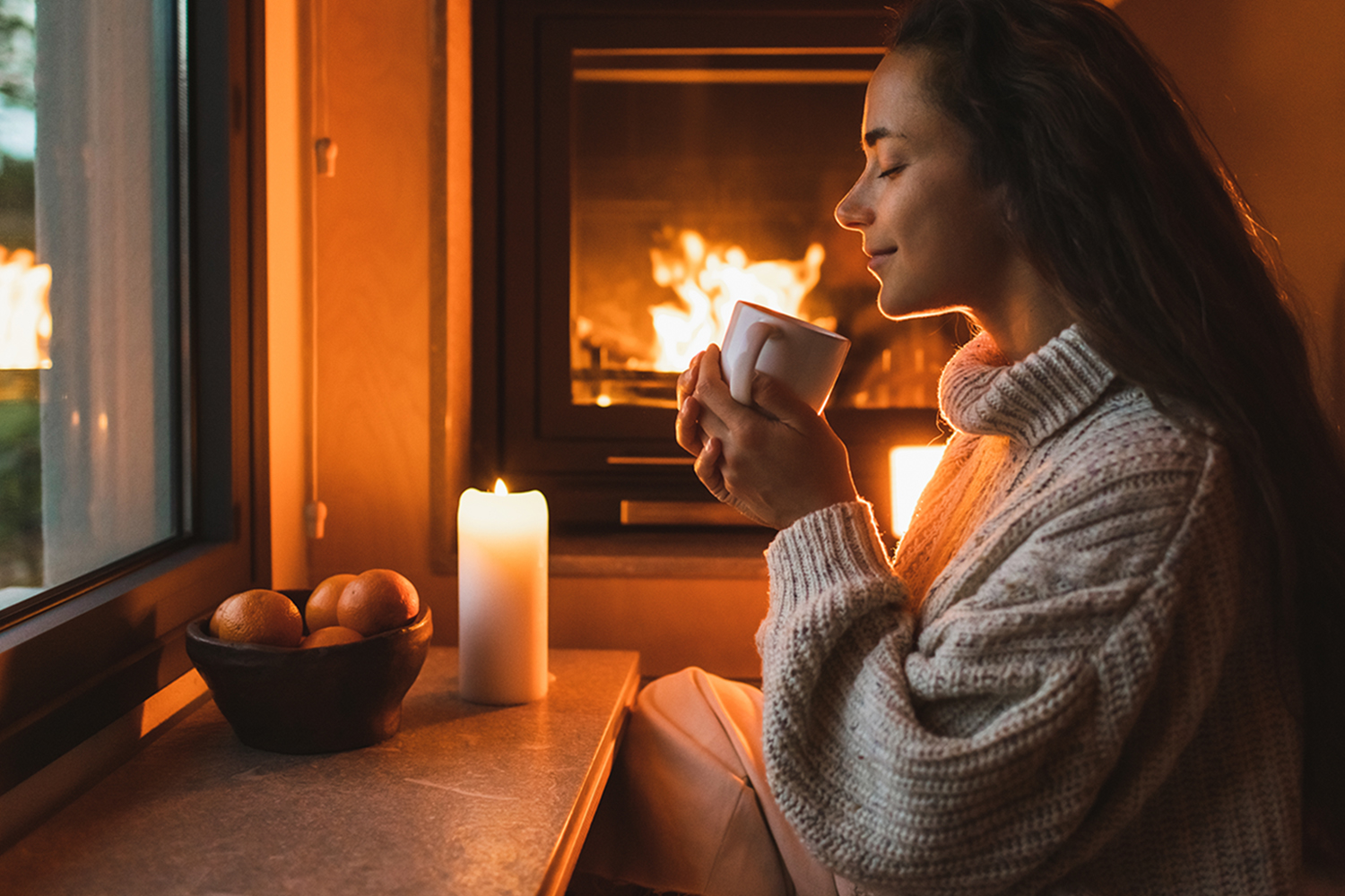 a woman enjoying the warmth of a fireplace and a hot drink