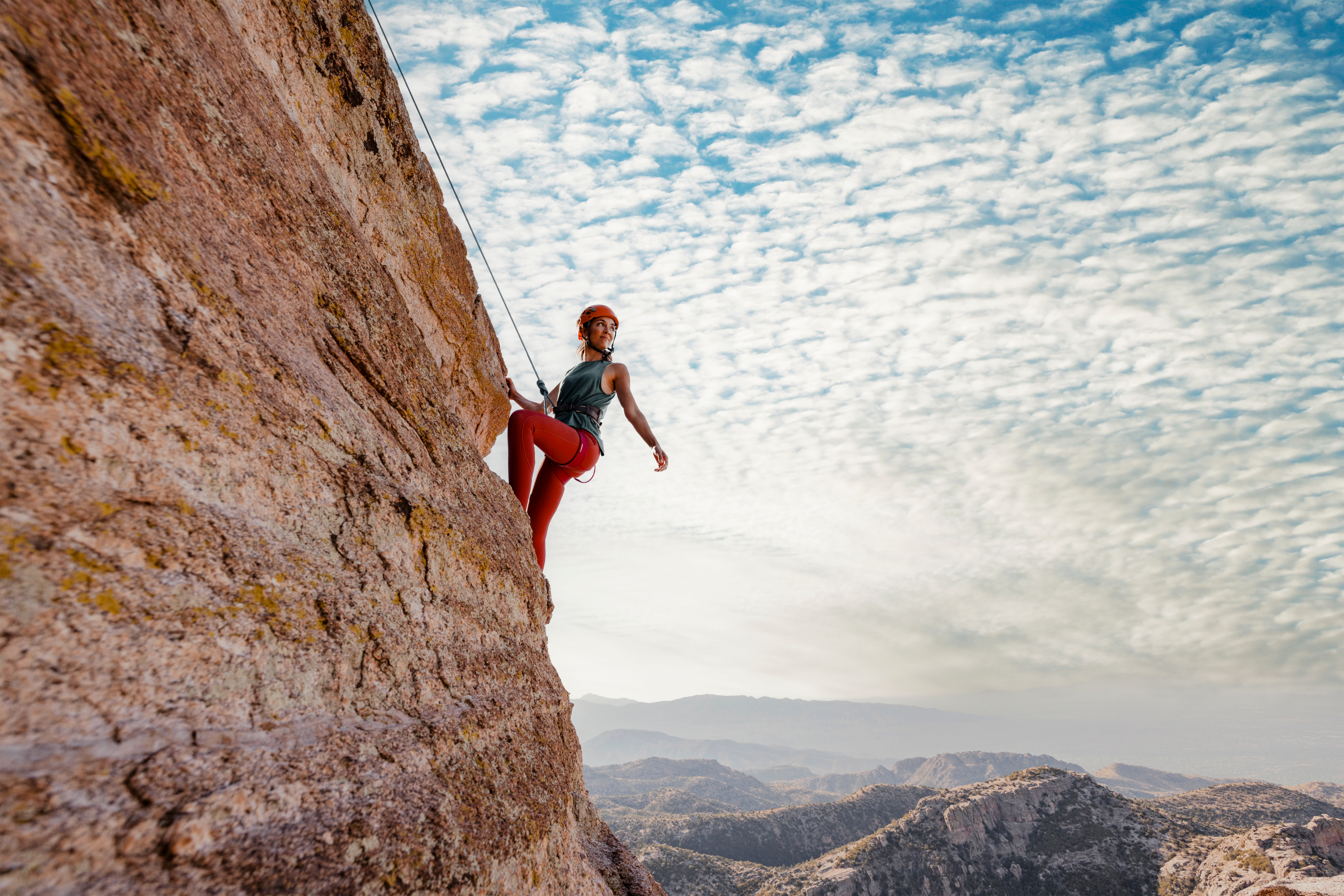 Woman having a great time while mountain climbing on side of rock.