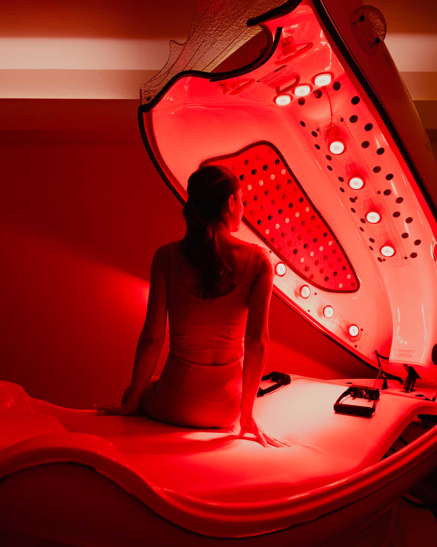 A woman in a red light infrared sauna pod