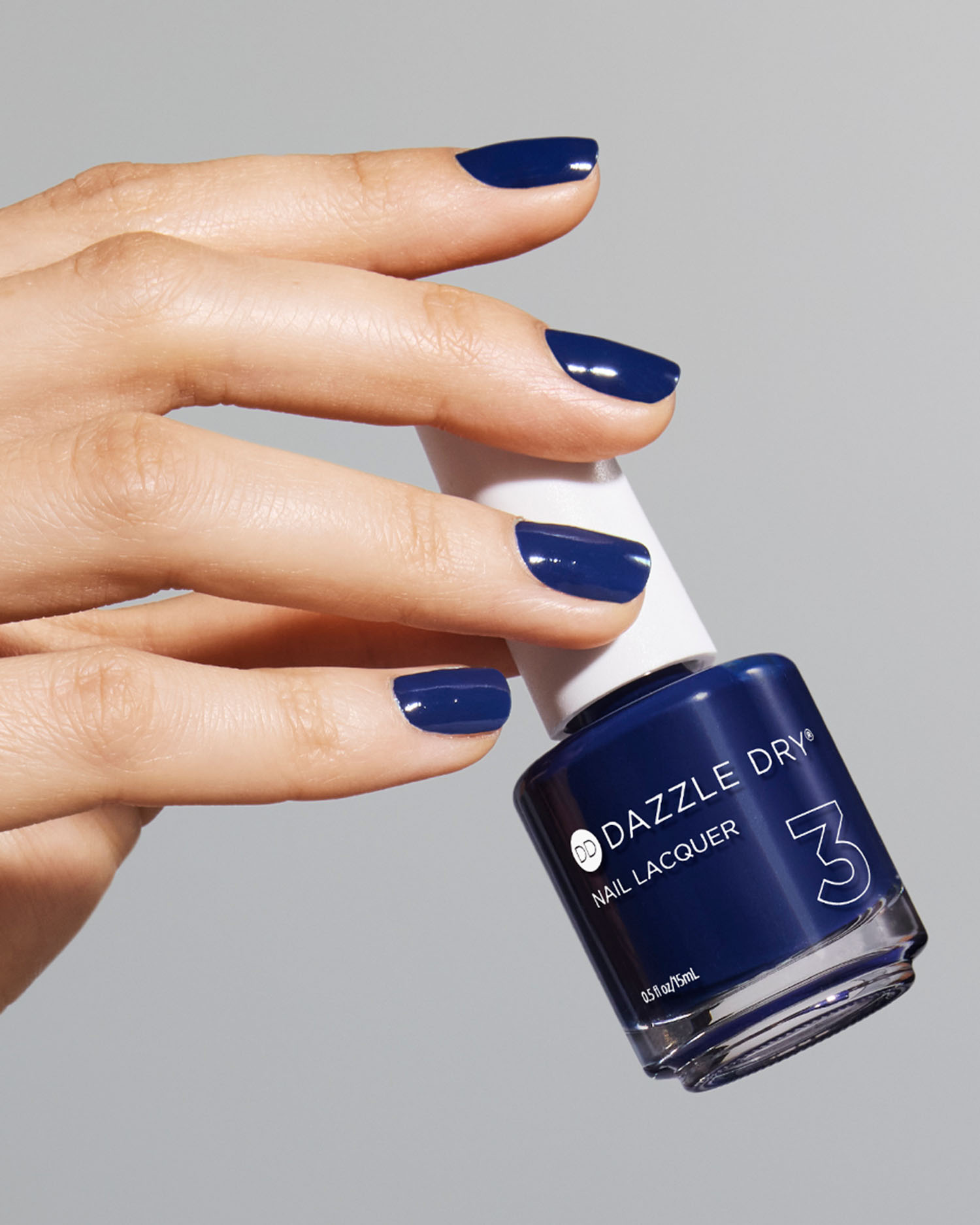 a manicured hand with blue nail polish holding a Dazzle Dry nail polish bottle