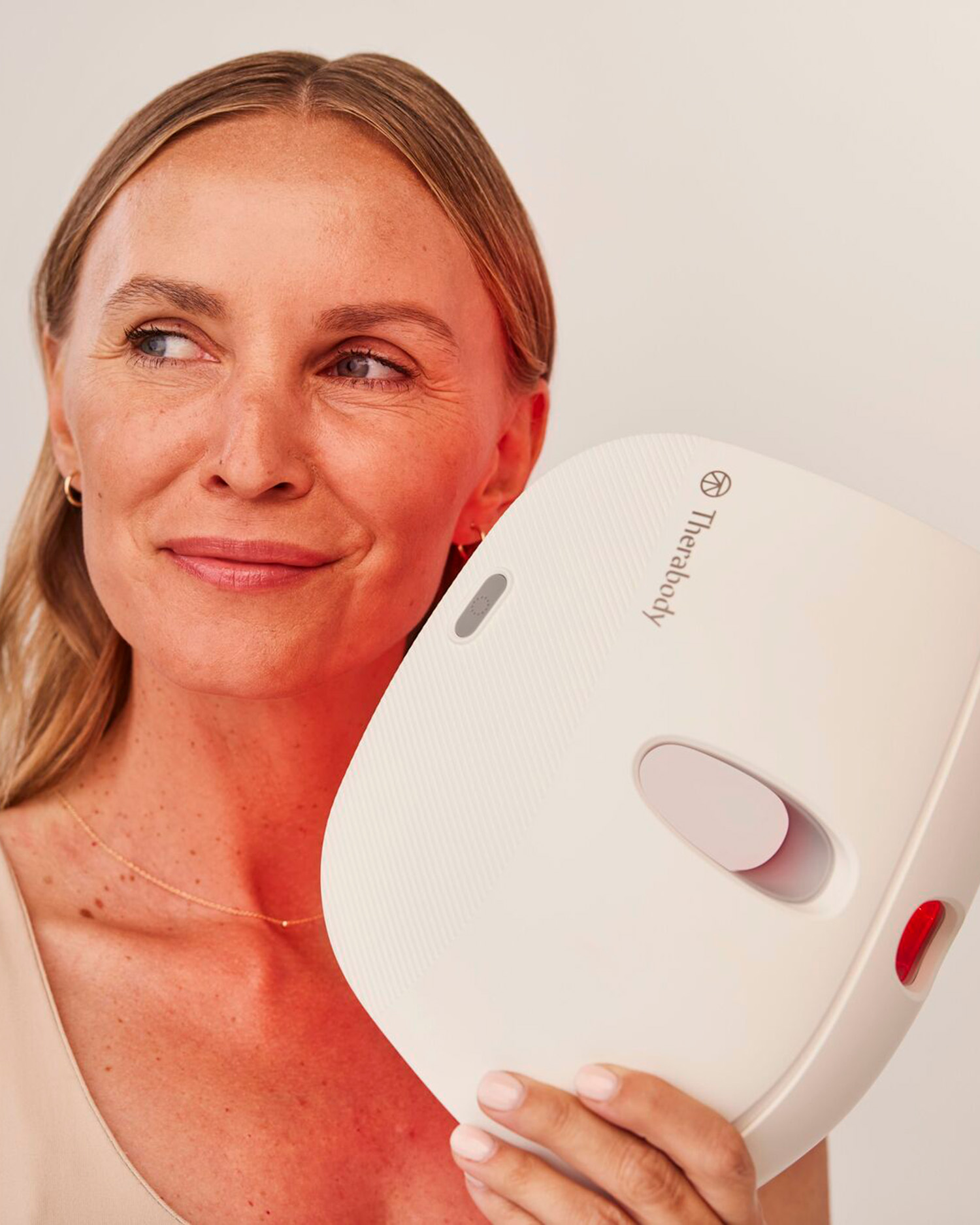 a woman holding a Therabody redlight mask near her face