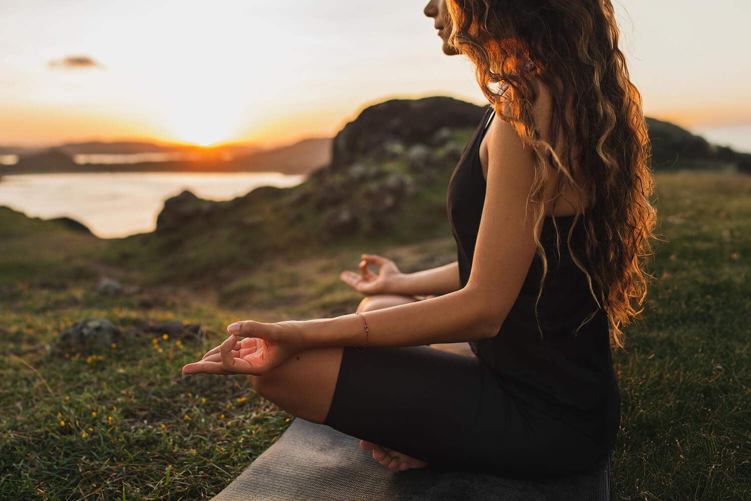 A woman meditating on a hill overlooking a lake