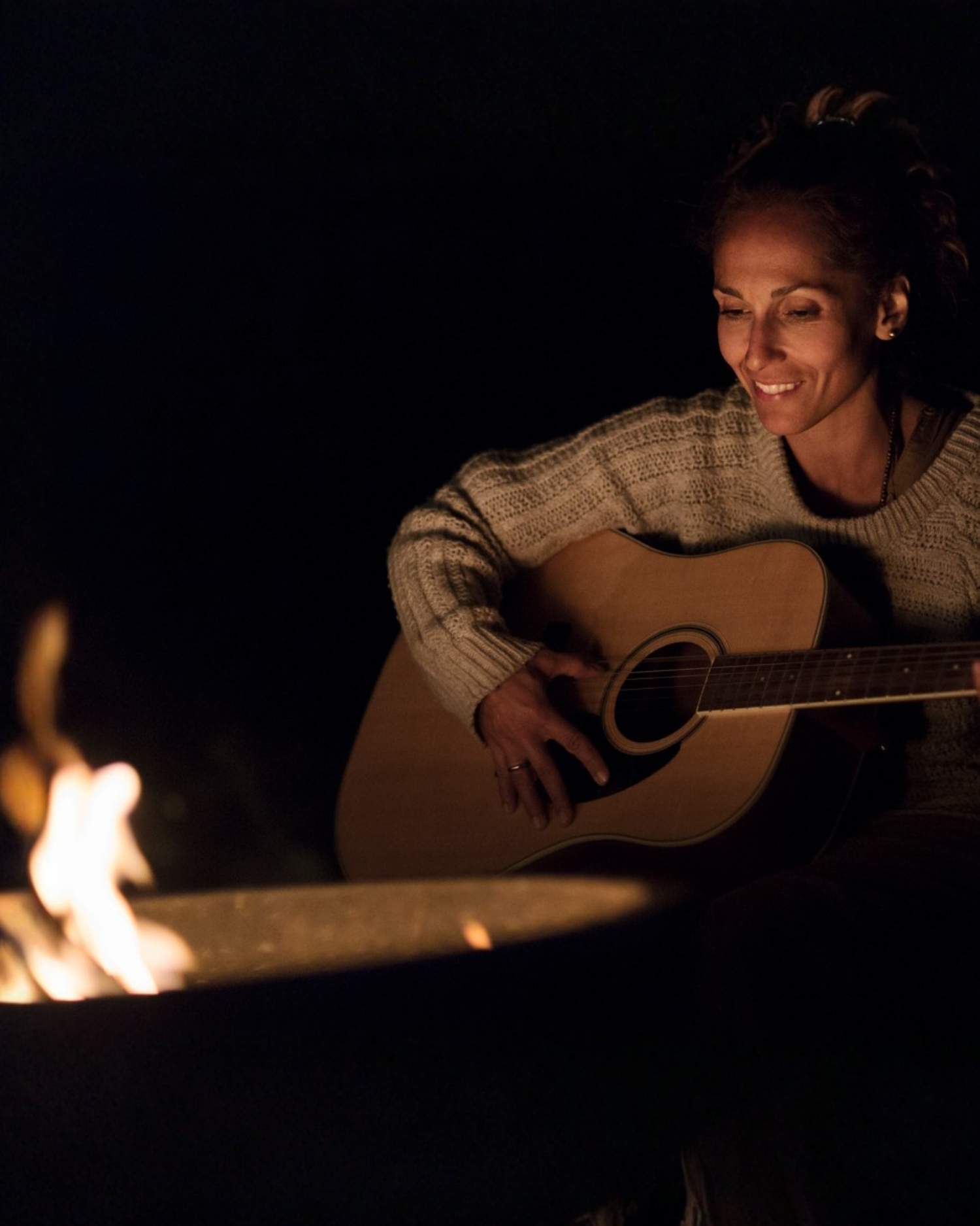 a woman playing guitar by the campfire