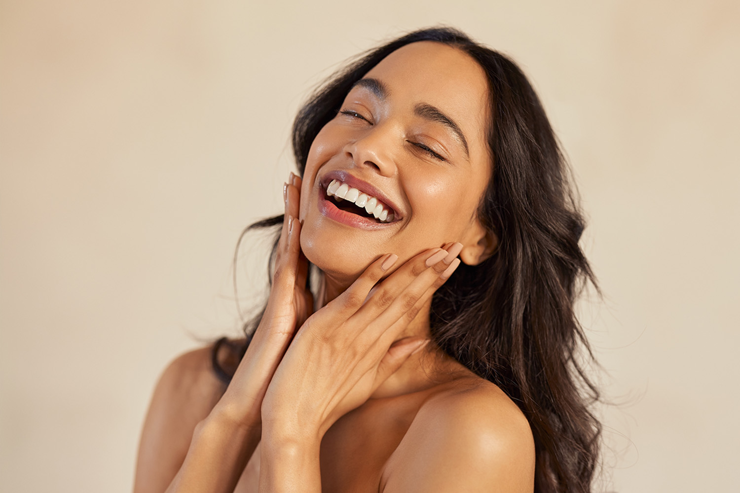 a woman smiling while she applies skin care products