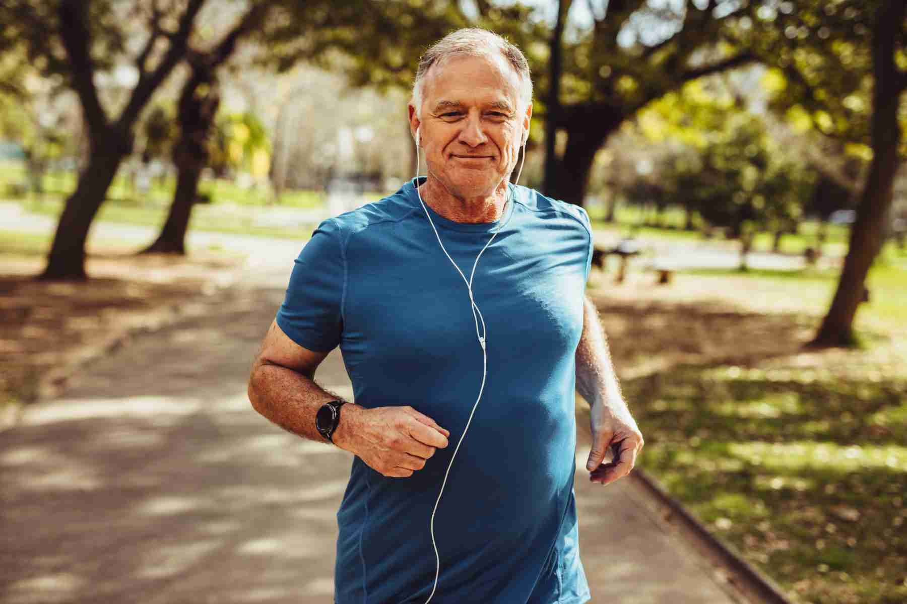 Older man running through park with headphones in.