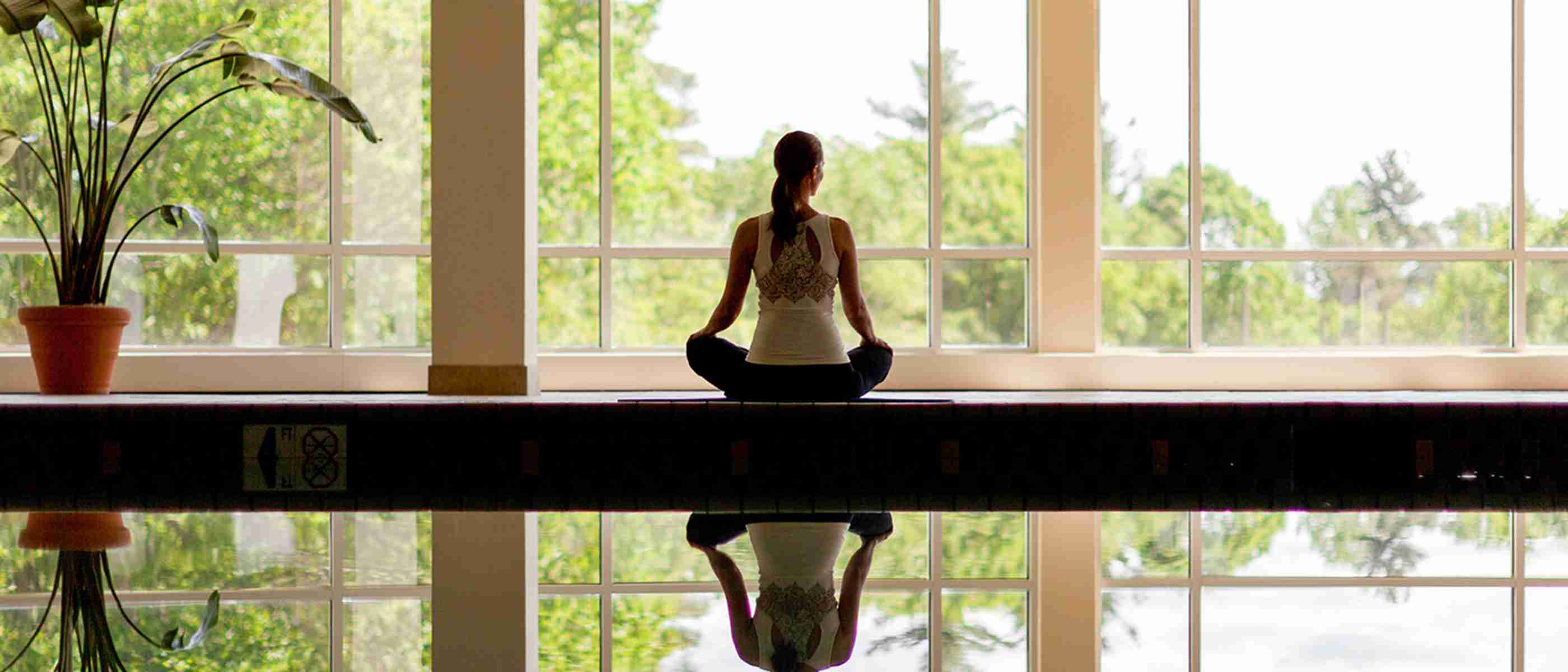 A woman sitting next to an indoor swimming pool meditating