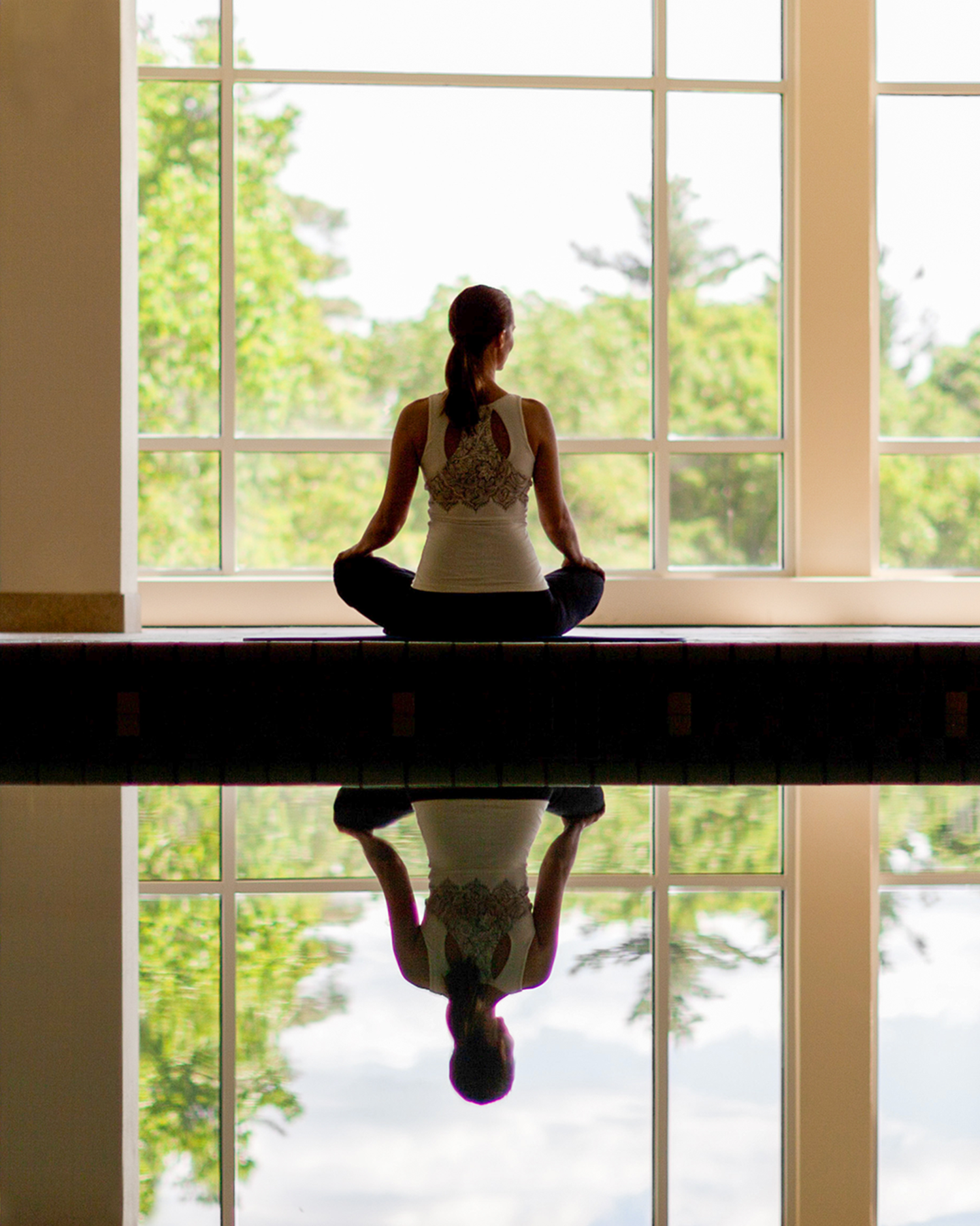 A woman sitting next to an indoor swimming pool meditating