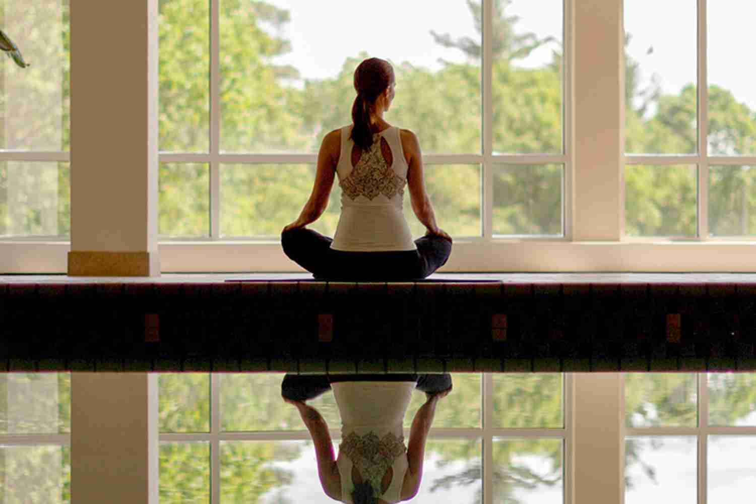 woman meditating in front of large windows
