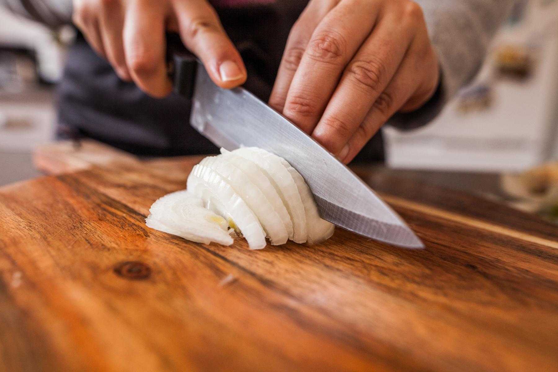 Close-up of hands chopping onions with knife.