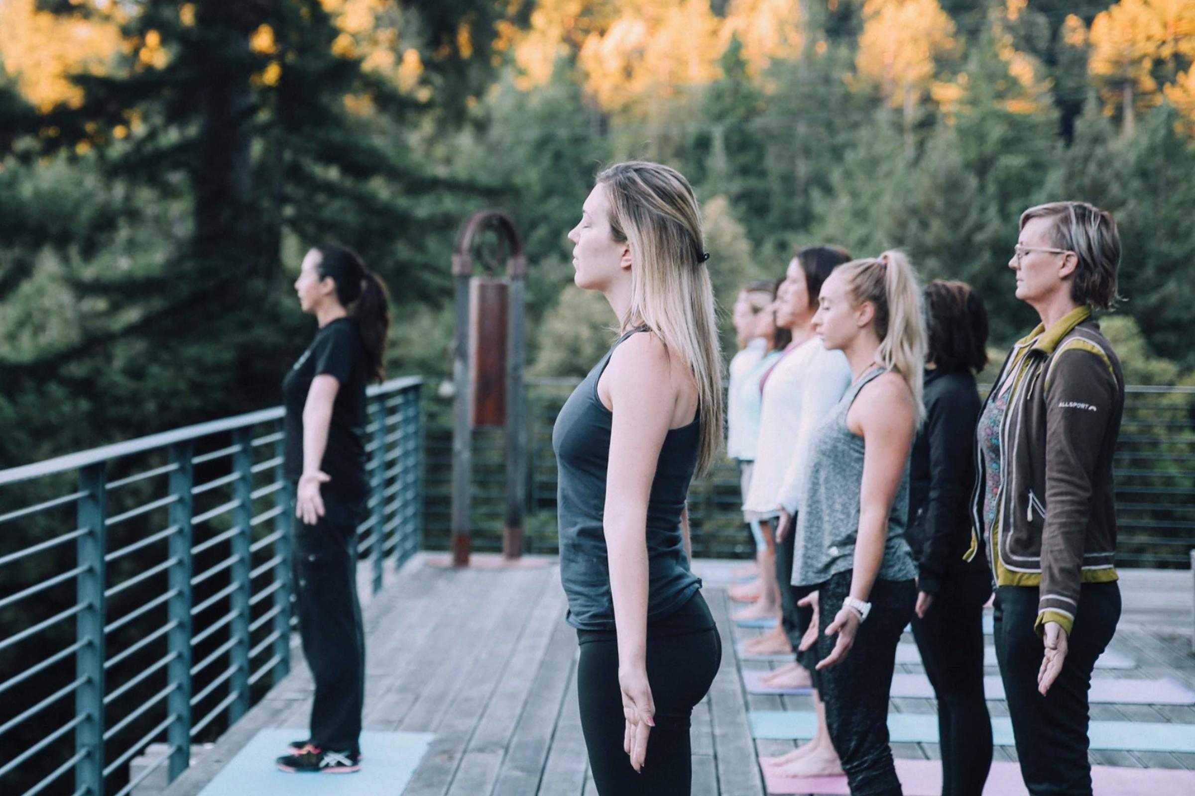 group of women doing yoga outside on deck overlooking green pine trees