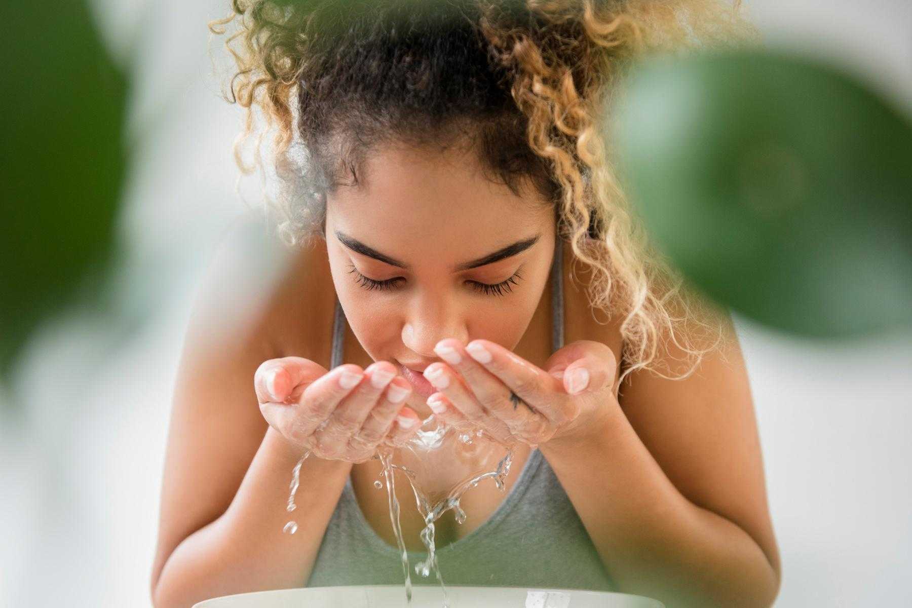 A young woman rinsing her face with water.