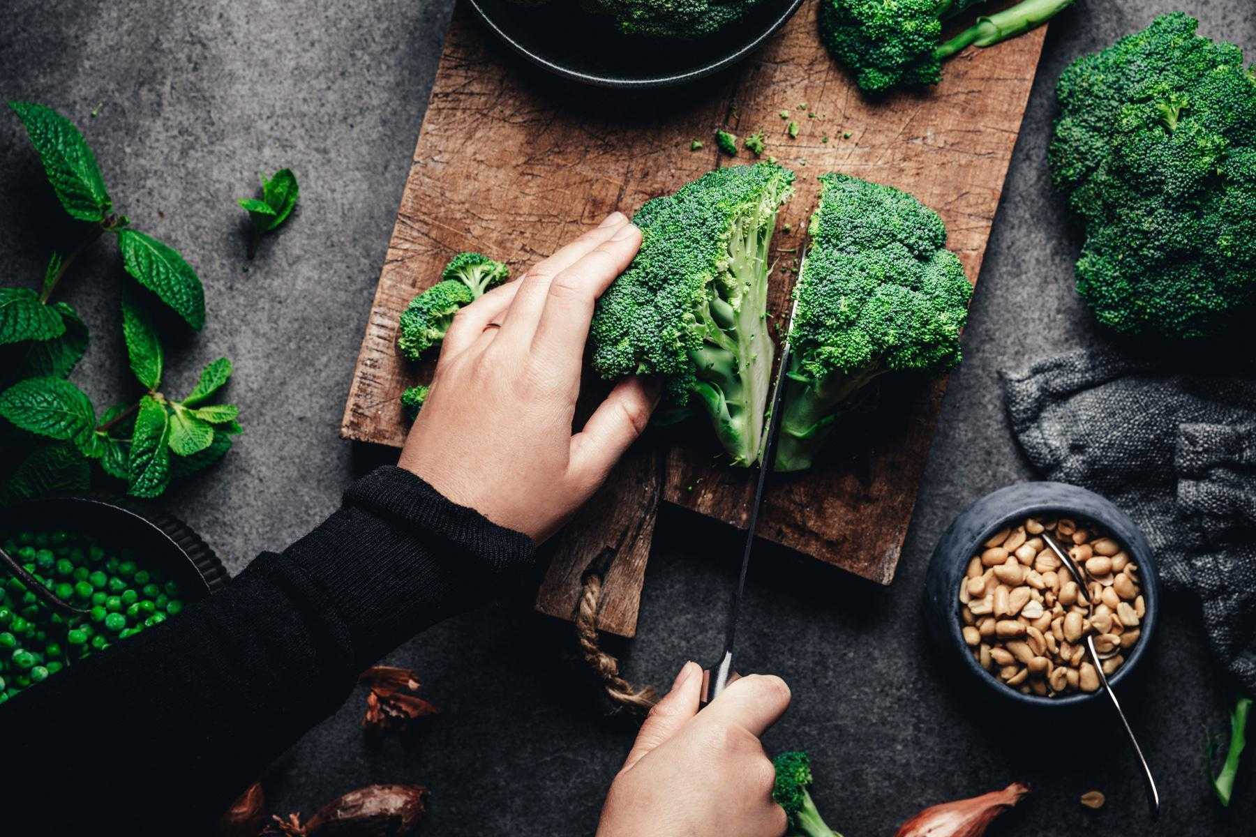 overhead shot of woman cutting broccoli on wooden cutting board