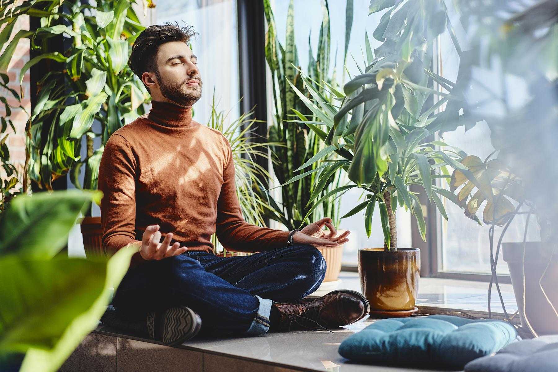 Man meditating surrounded by plants.