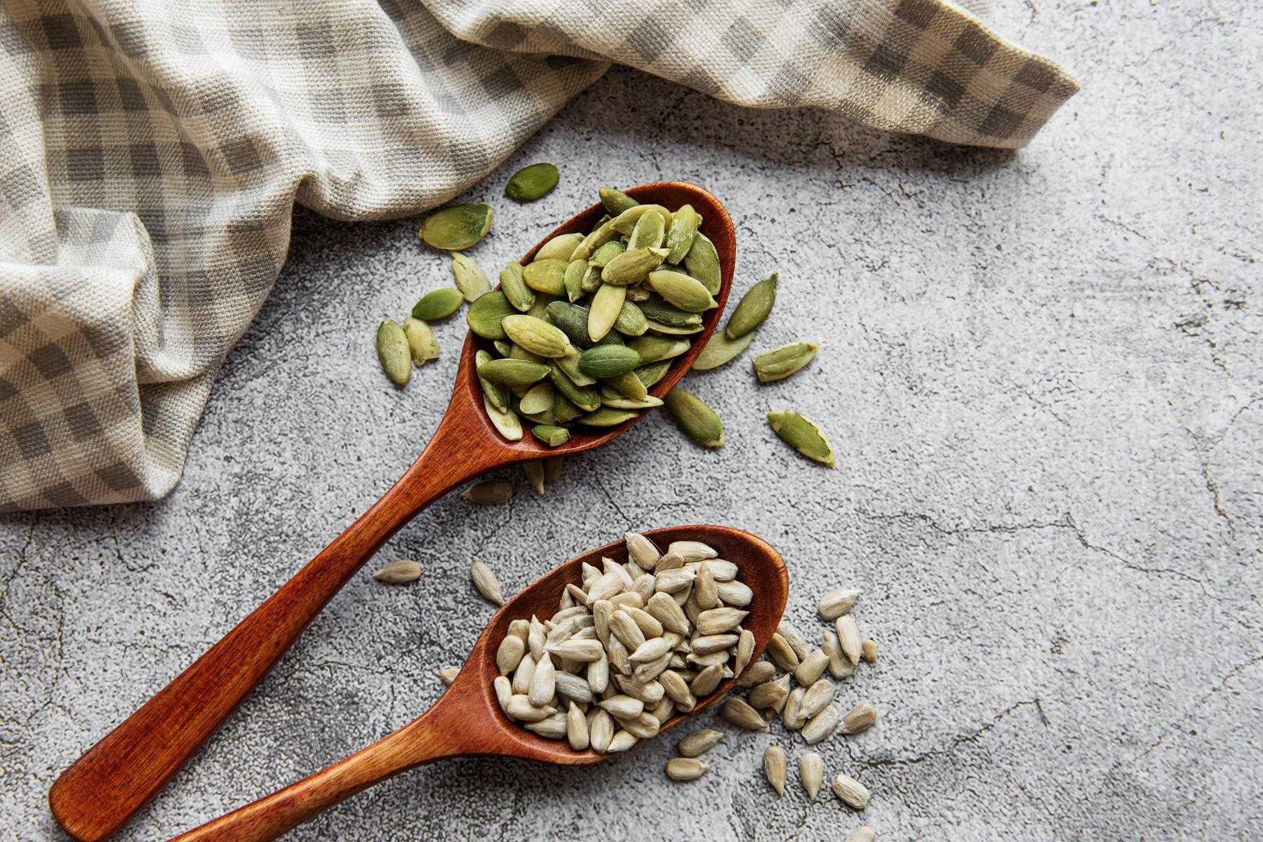 Close-up of pumpkin and sunflower seeds in wooden spoons.