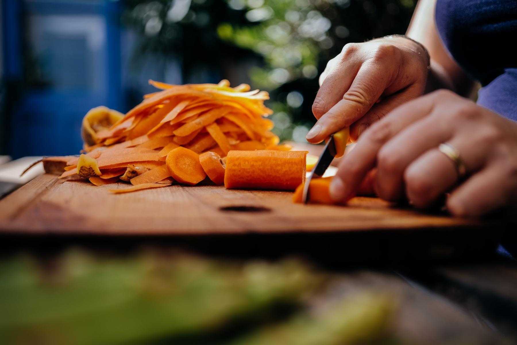 Close-up of man chopping carrots on wooden cutting board.