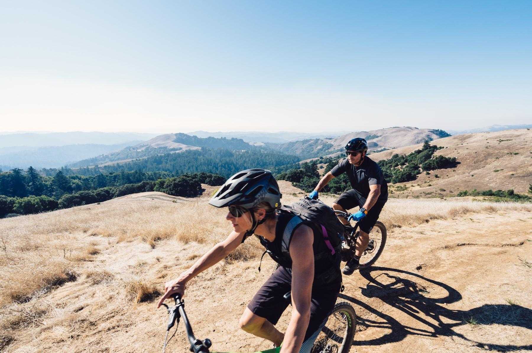 action shot of man and woman on mountain bikes as they ride at the top of a mount range