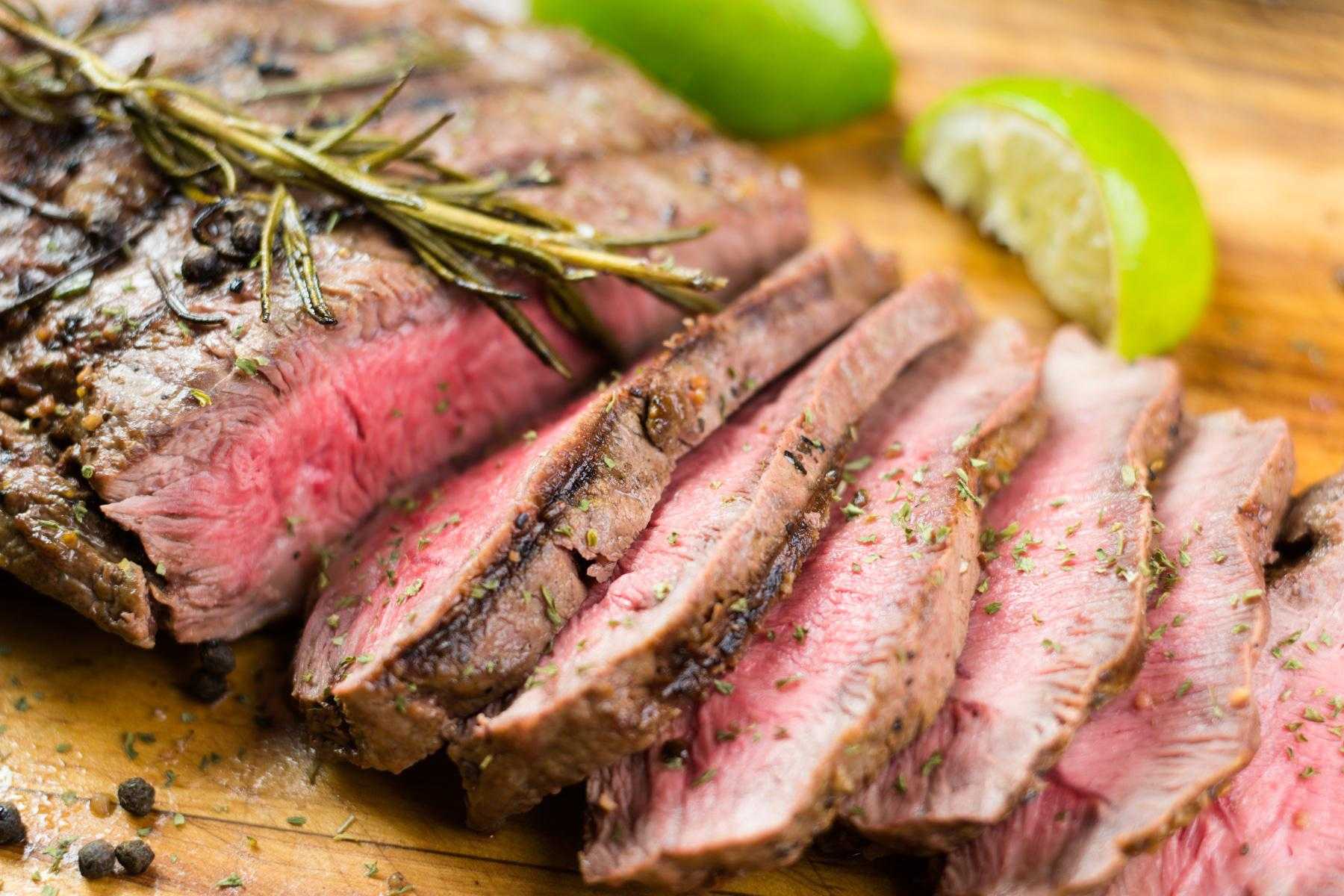Close-up of sliced lamb on a wooden cutting board.