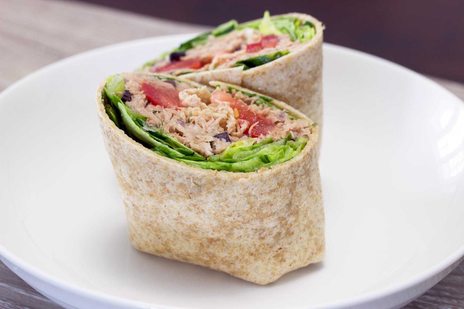 Close-up of a tuna salad wrap cut in half on a white plate.