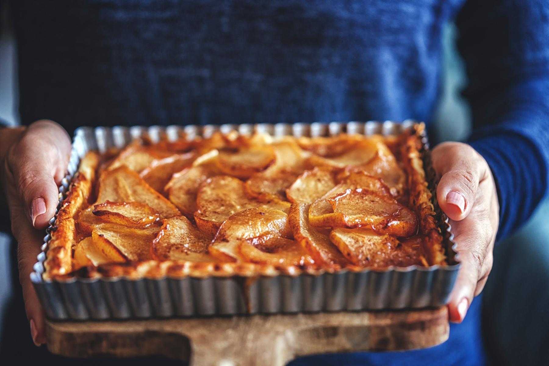 Close-up of woman holding freshly baked almond pear torte.
