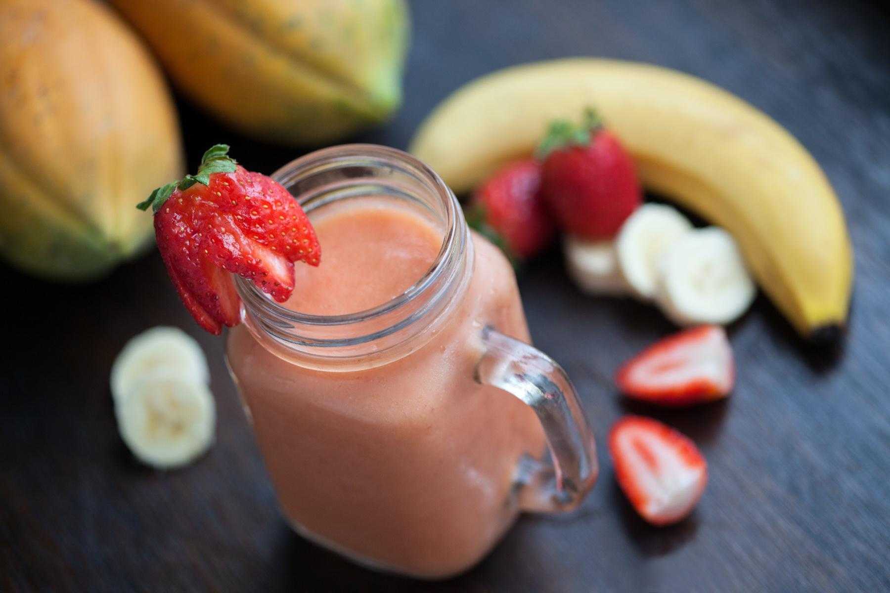 A countertop with strawberry and banana pieces and a mason jar filled with a strawberry banana smoothie.