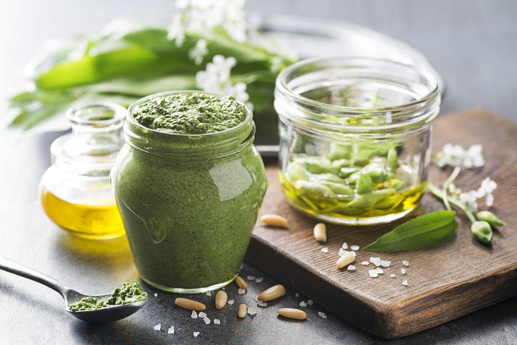 Close-up image of Basil Pine Nut Pesto in a jar with ingredients.