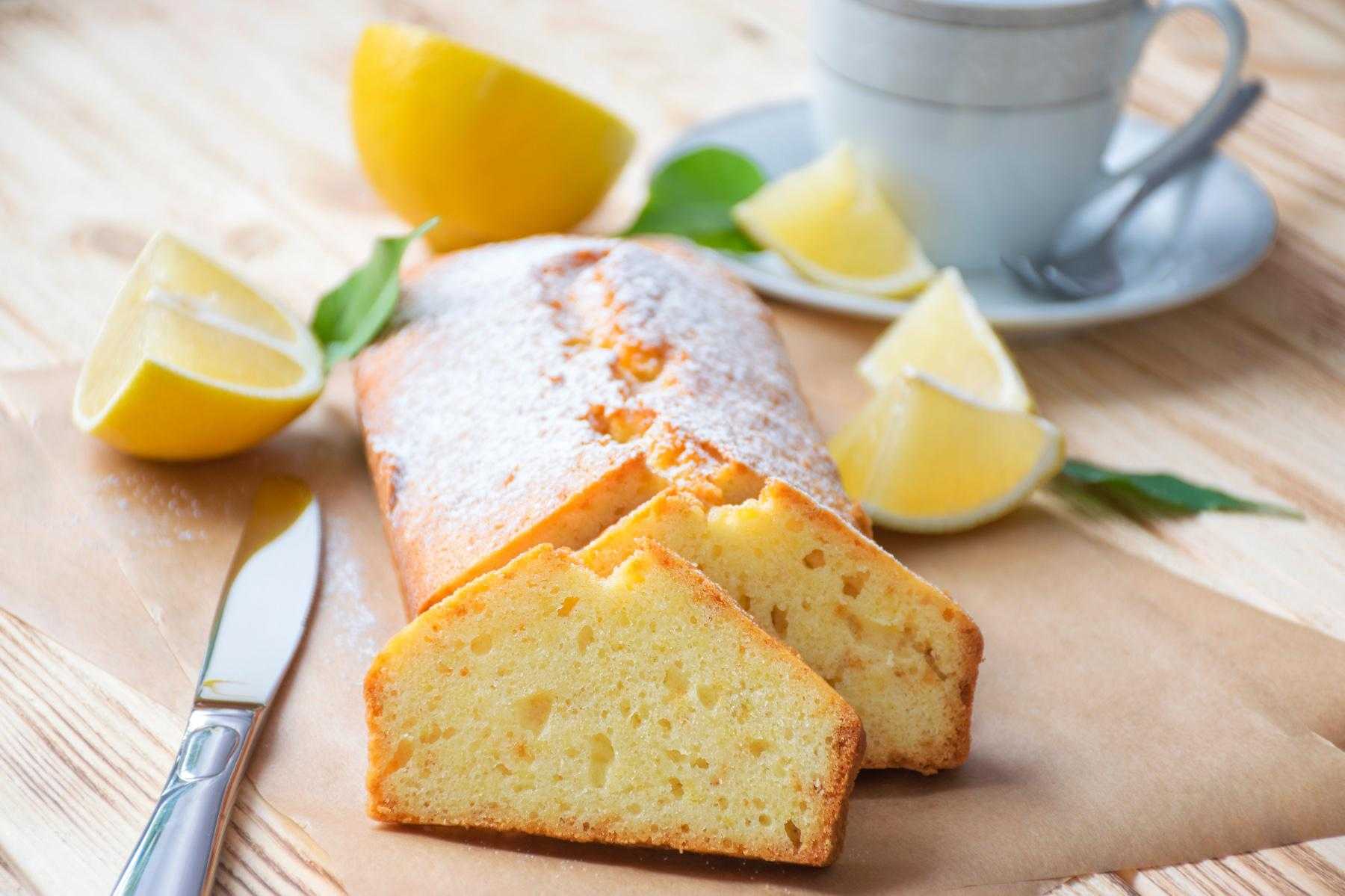 A loaf of lemon pound cake cut into slices on wooden cutting board.