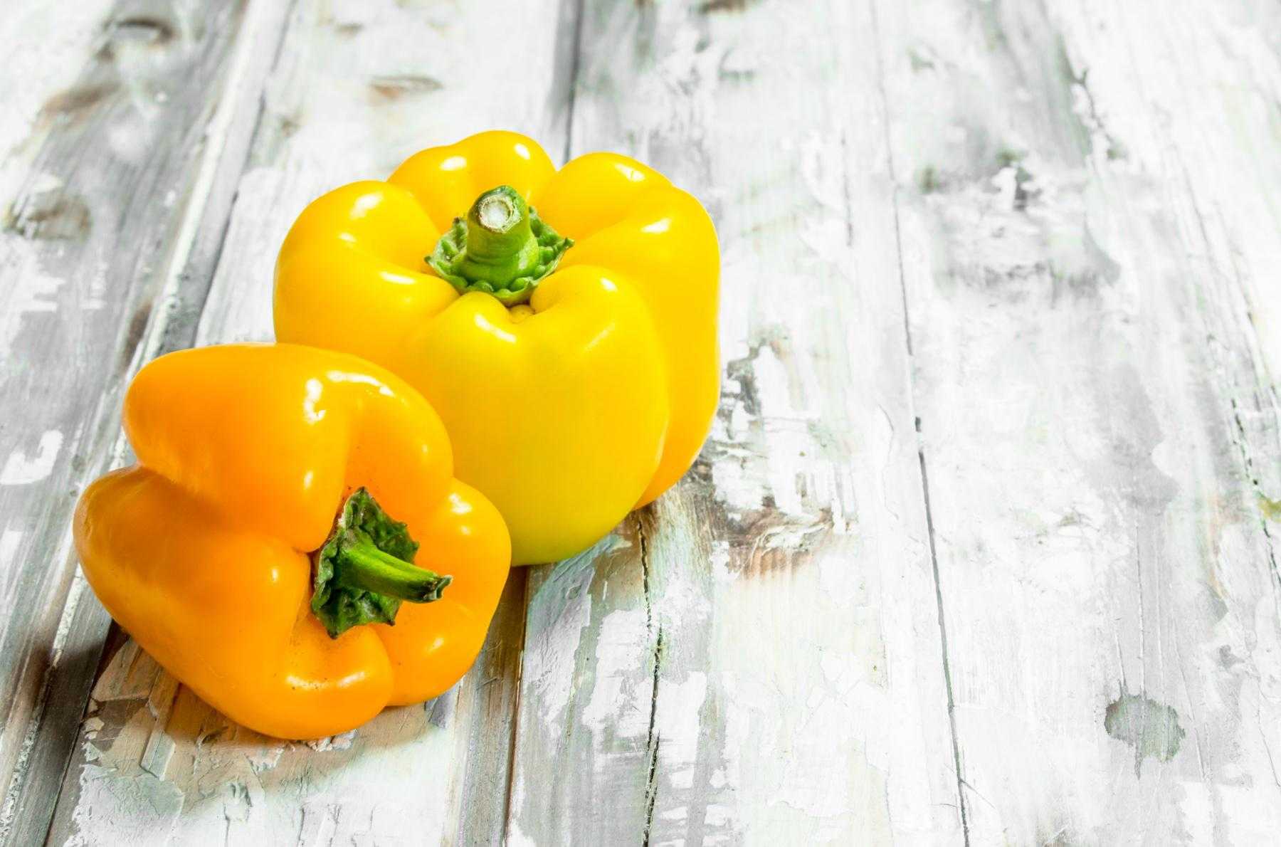 Two yellow bell peppers on a wooden table.