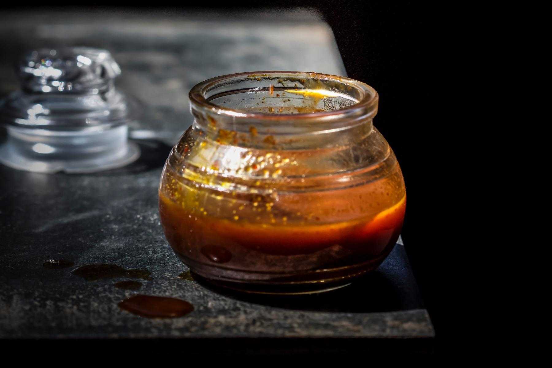 Glass jar of hoisin sauce on black table.