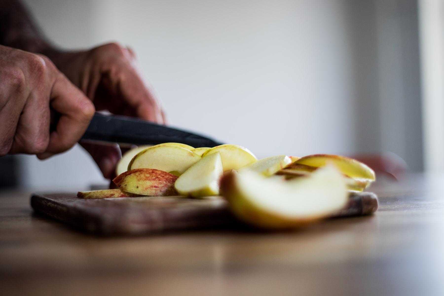 Close-up of hands chopping apple with knife from side.