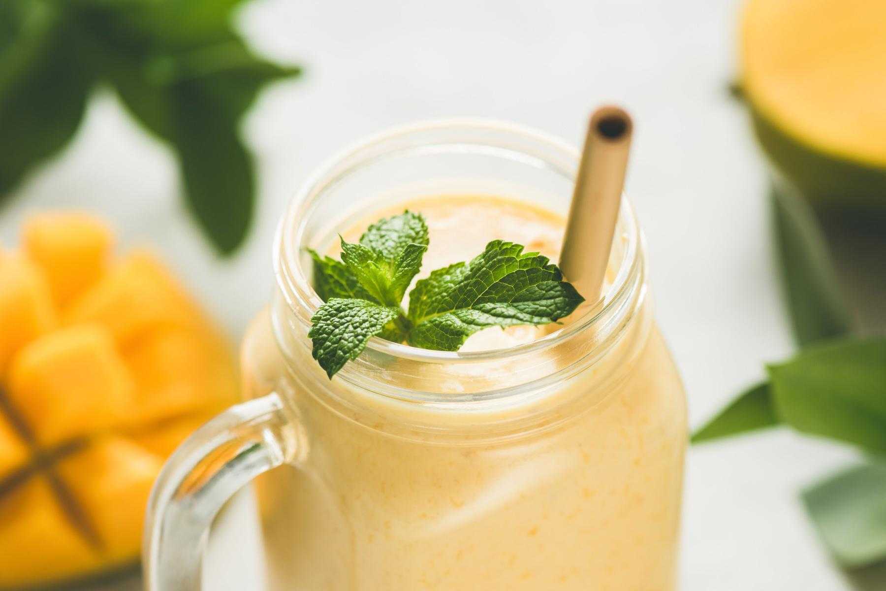 Close-up of mango and papaya smoothie in a glass jar with straw.