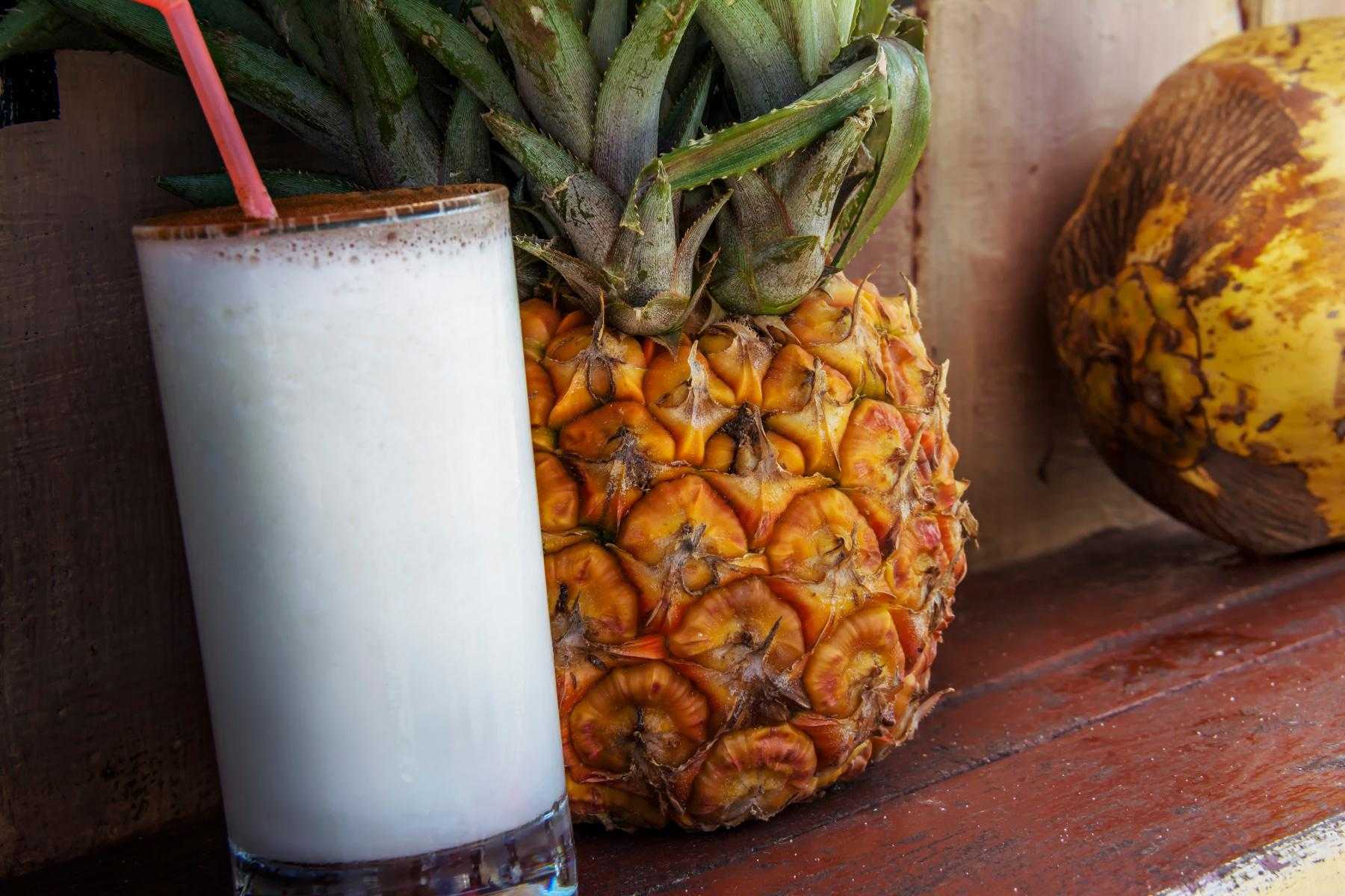 Pina colada smoothie in glass next to pineapple.